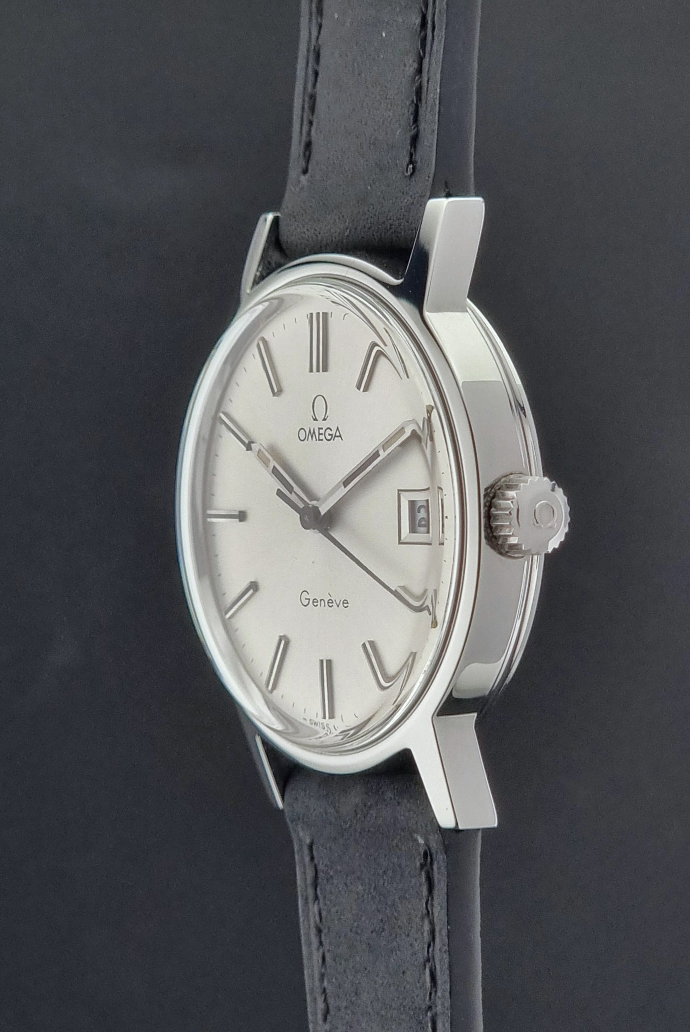 Vintage Omega Geneve watch with silver dial and black leather strap on a dark background
