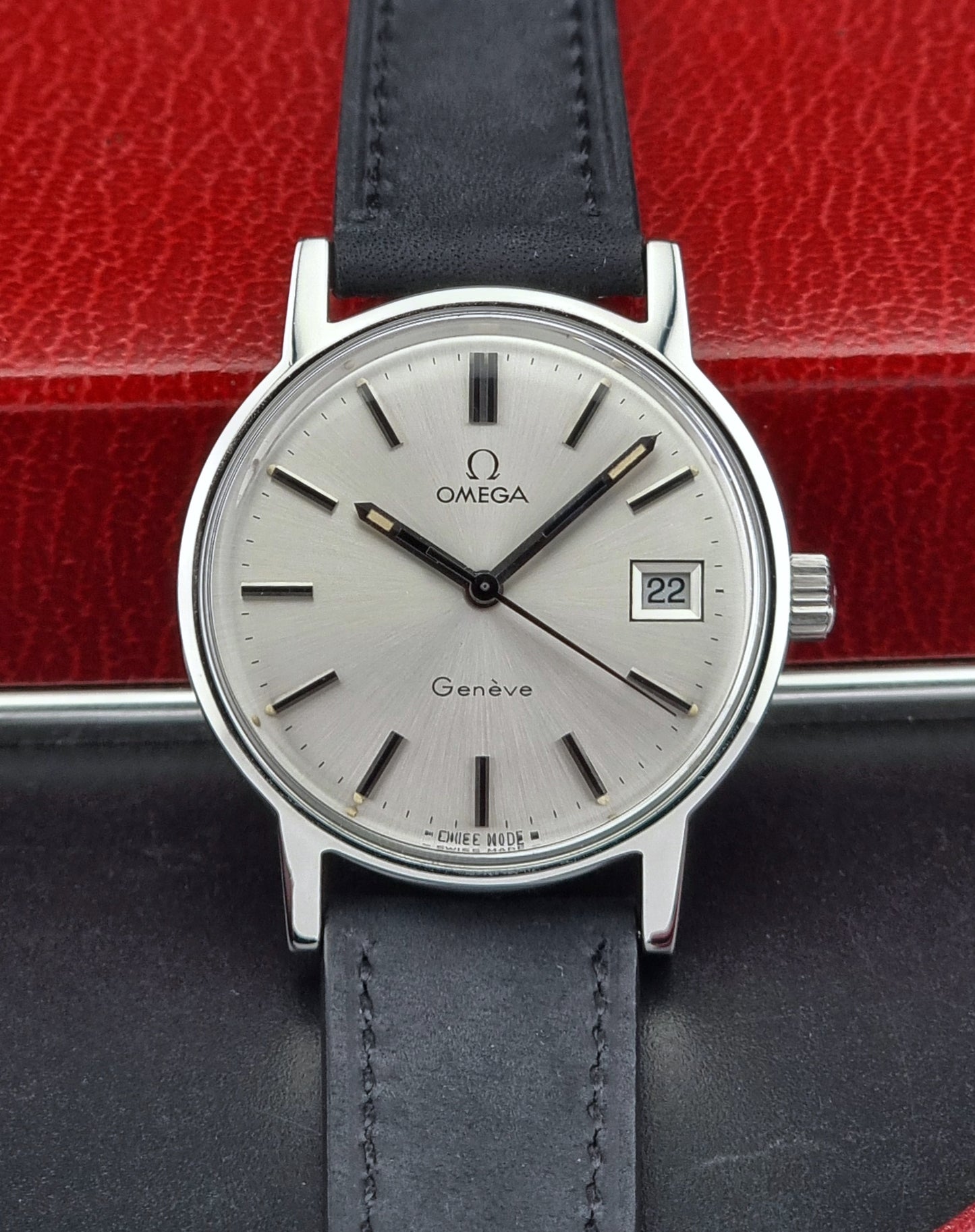 Vintage Omega Geneve watch with black leather strap on a red and black background