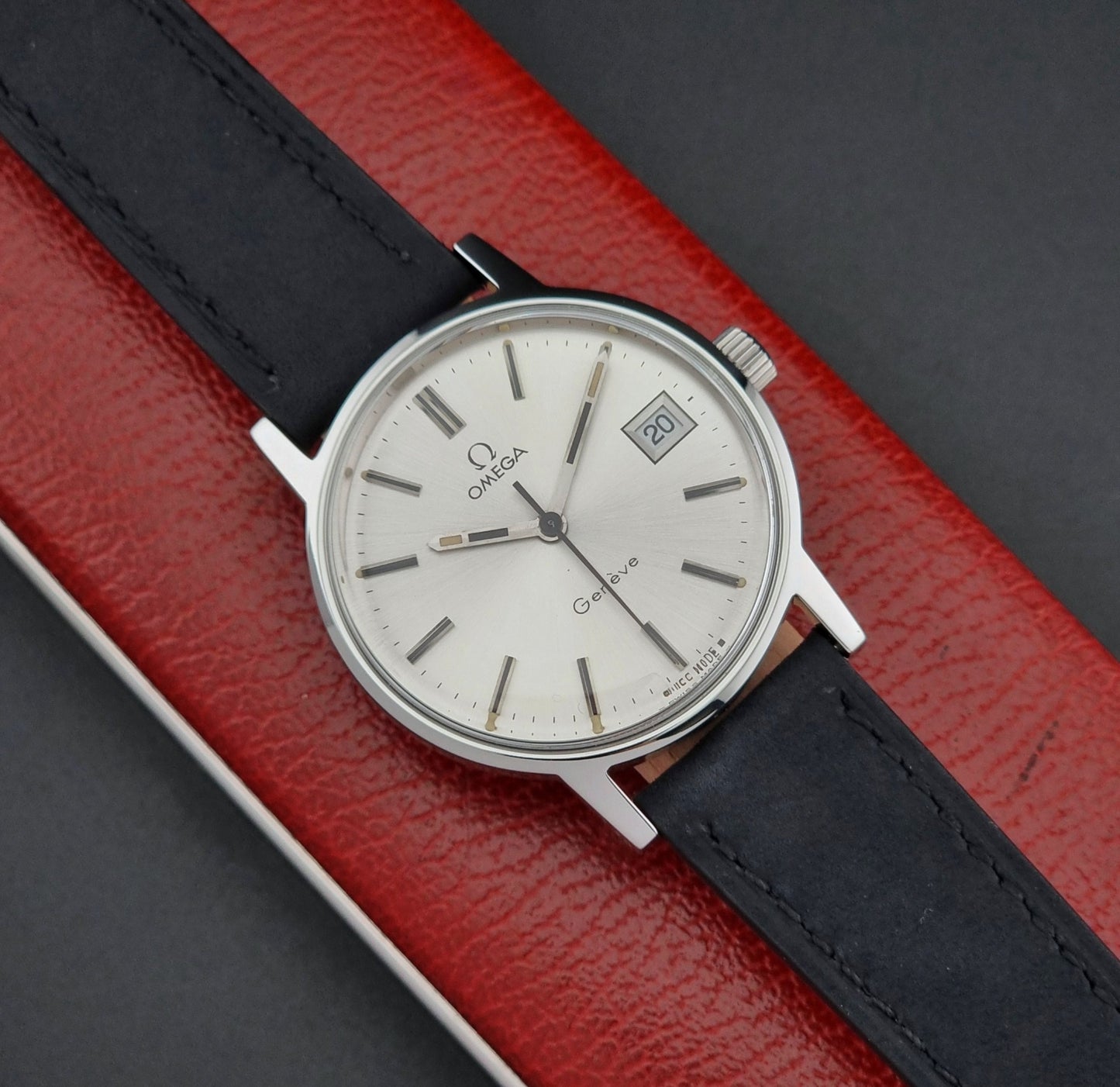 Vintage Omega Geneve watch with black strap on a red and gray background