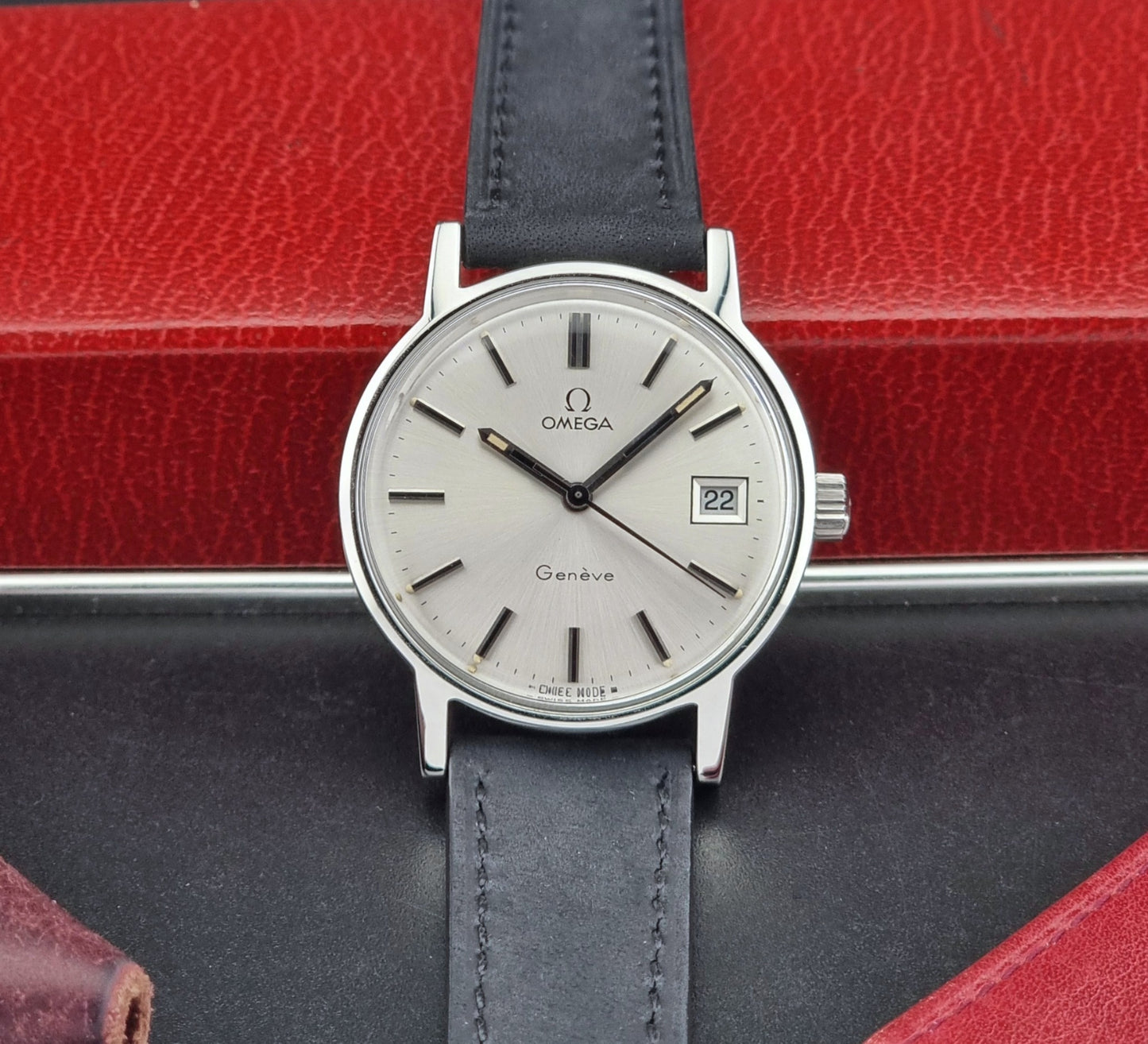 Vintage Omega Geneve watch with black leather strap on a red and black background