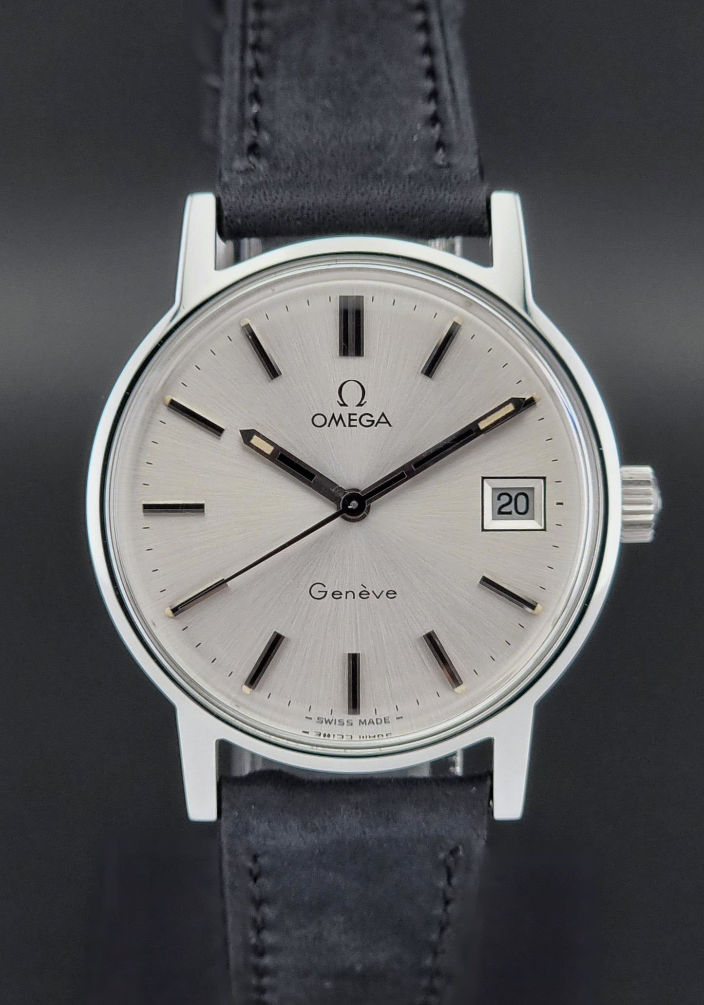 Vintage Omega Geneve watch with silver case and blue leather strap on a dark background