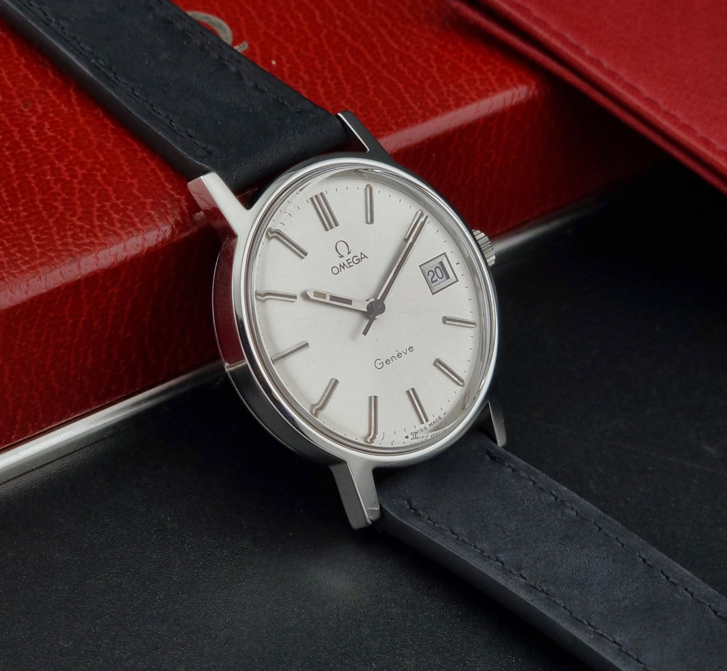 Vintage Omega Geneve watch with black strap on a dark surface with red background