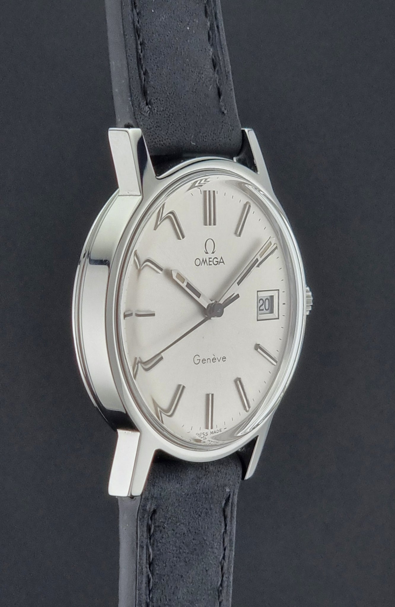 Vintage Omega Geneve watch with silver dial and black leather strap on a dark background