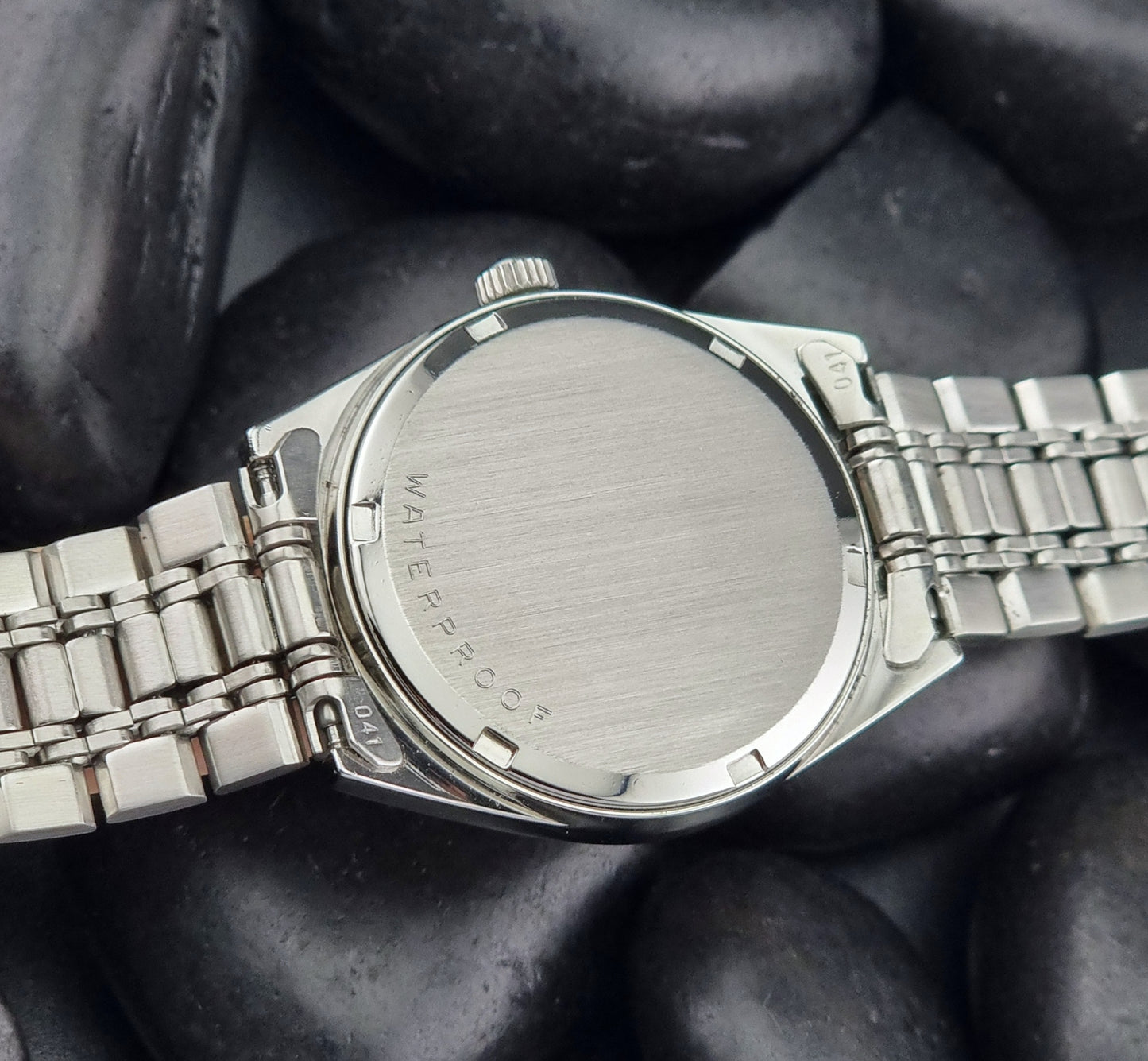 Vintage Omega Geneve watch with 'Waterproof' text on a dark stone surface