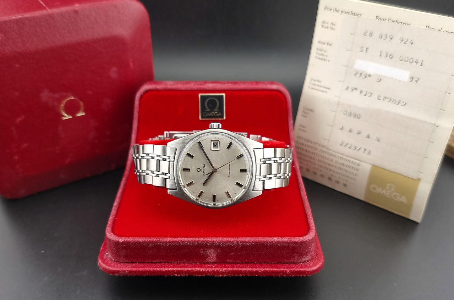 Vintage Omega Geneve watch on a red cushion with a red box and paper in the background