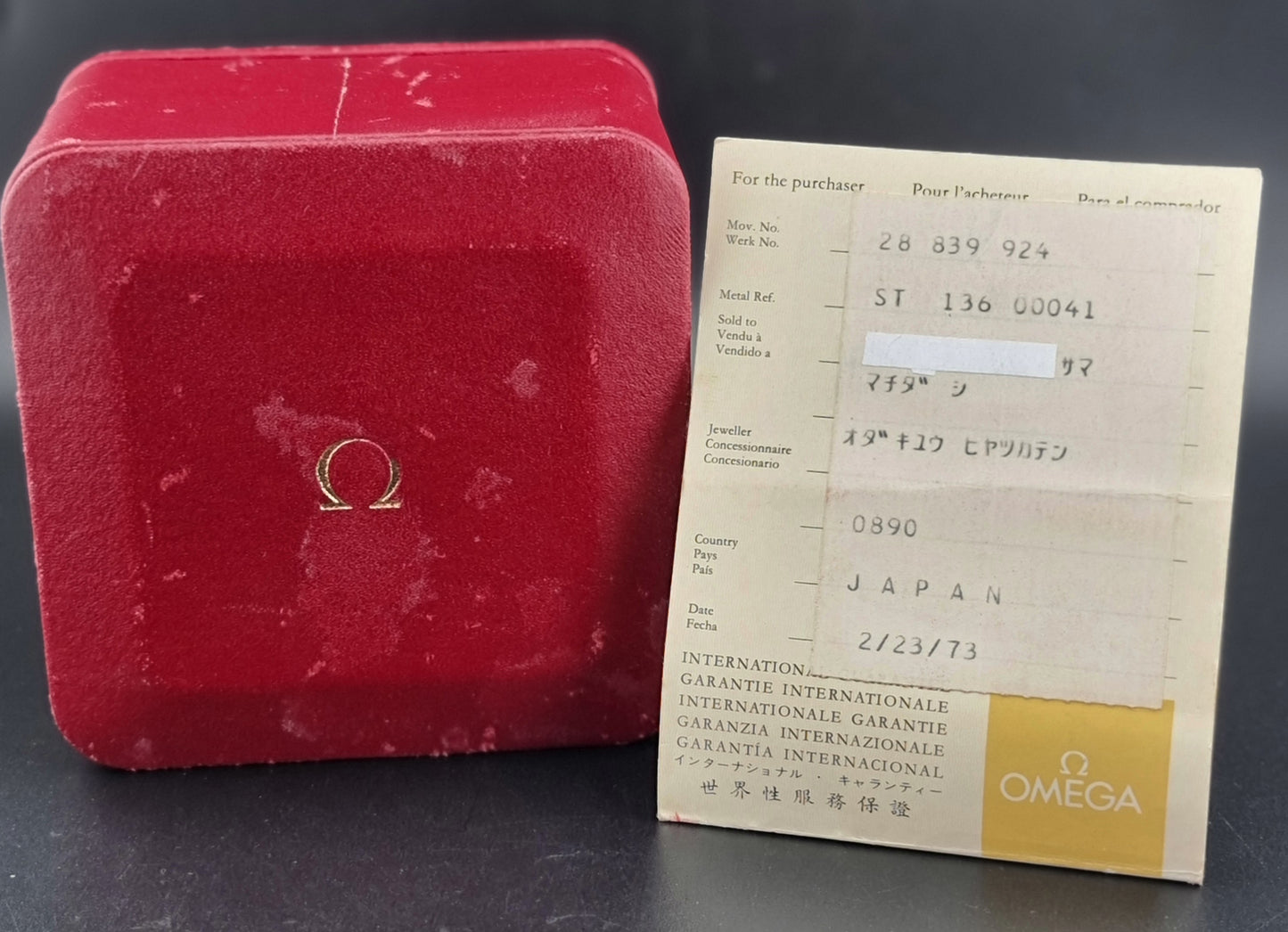 Red watch box with Omega logo and a warranty card on a dark surface