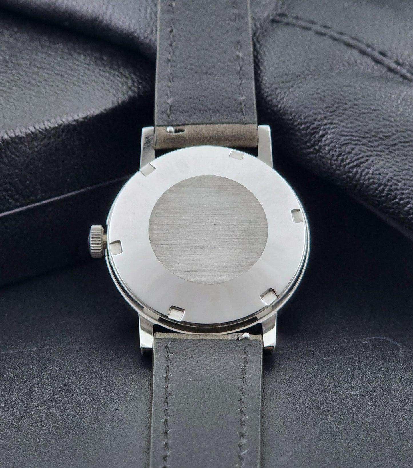 Vintage Omega Wristwatch Geneve 166.0098 with grey leather strap on a dark textured surface case back view