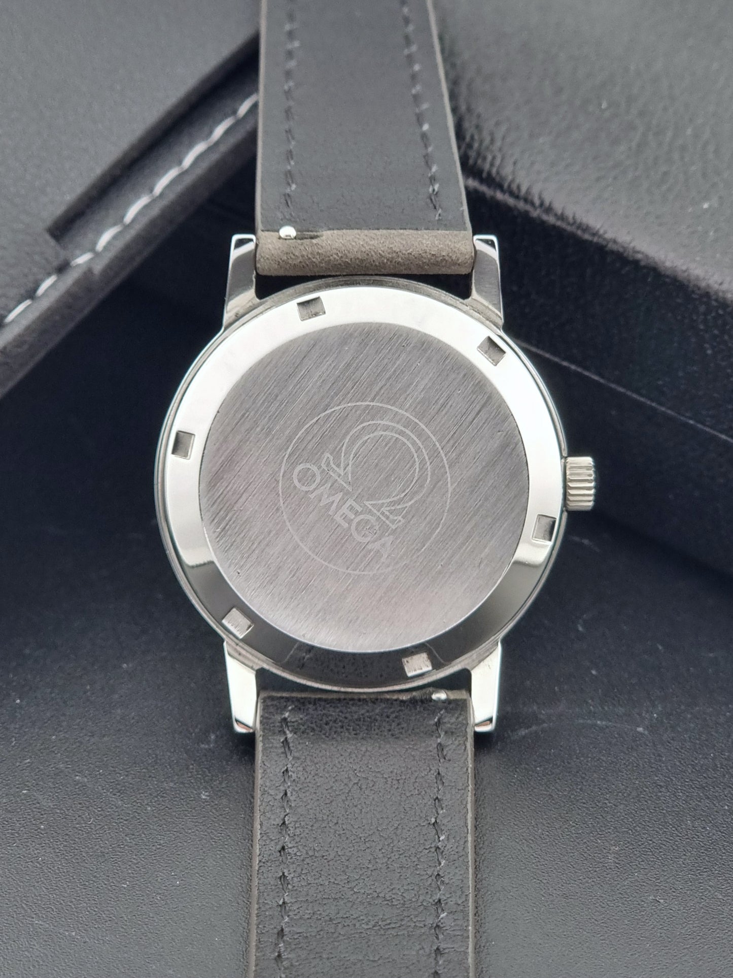 Vintage Omega Geneve 166.0163 watch with gray leather strap on a dark background case back view