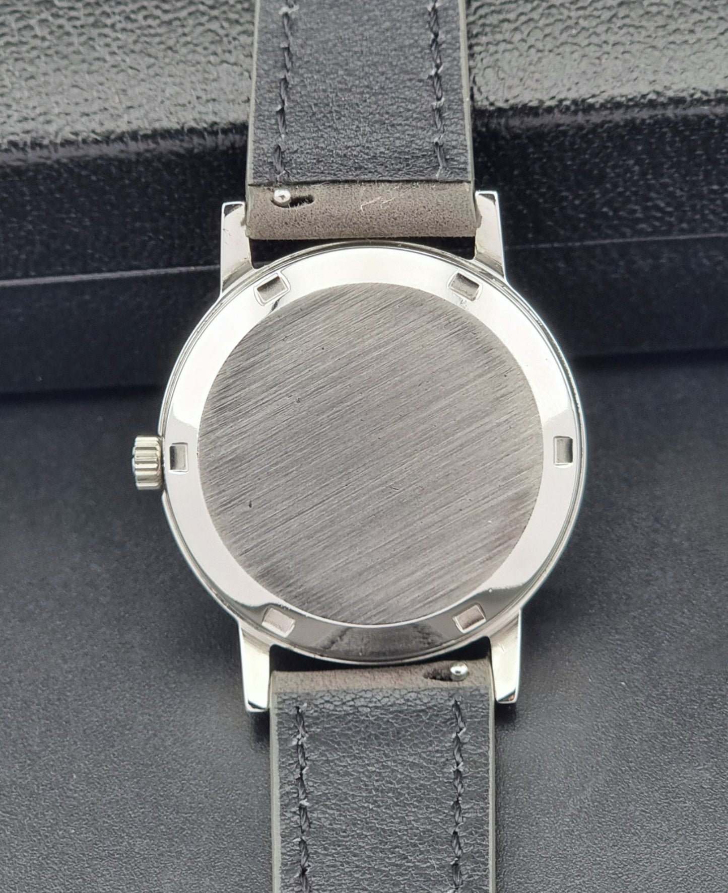 Vintage Omega case back with gray leather strap.