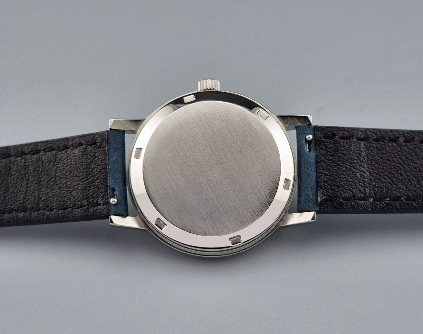 Vintage Omega Geneve 166.0163 wristwatch with black leather strap and silver case on a gray background