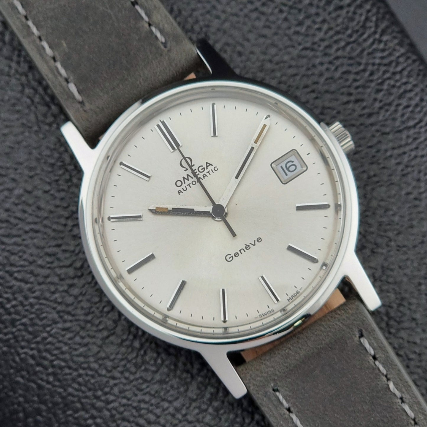 Vintage Omega watch with a silver case and gray leather strap on a textured gray background