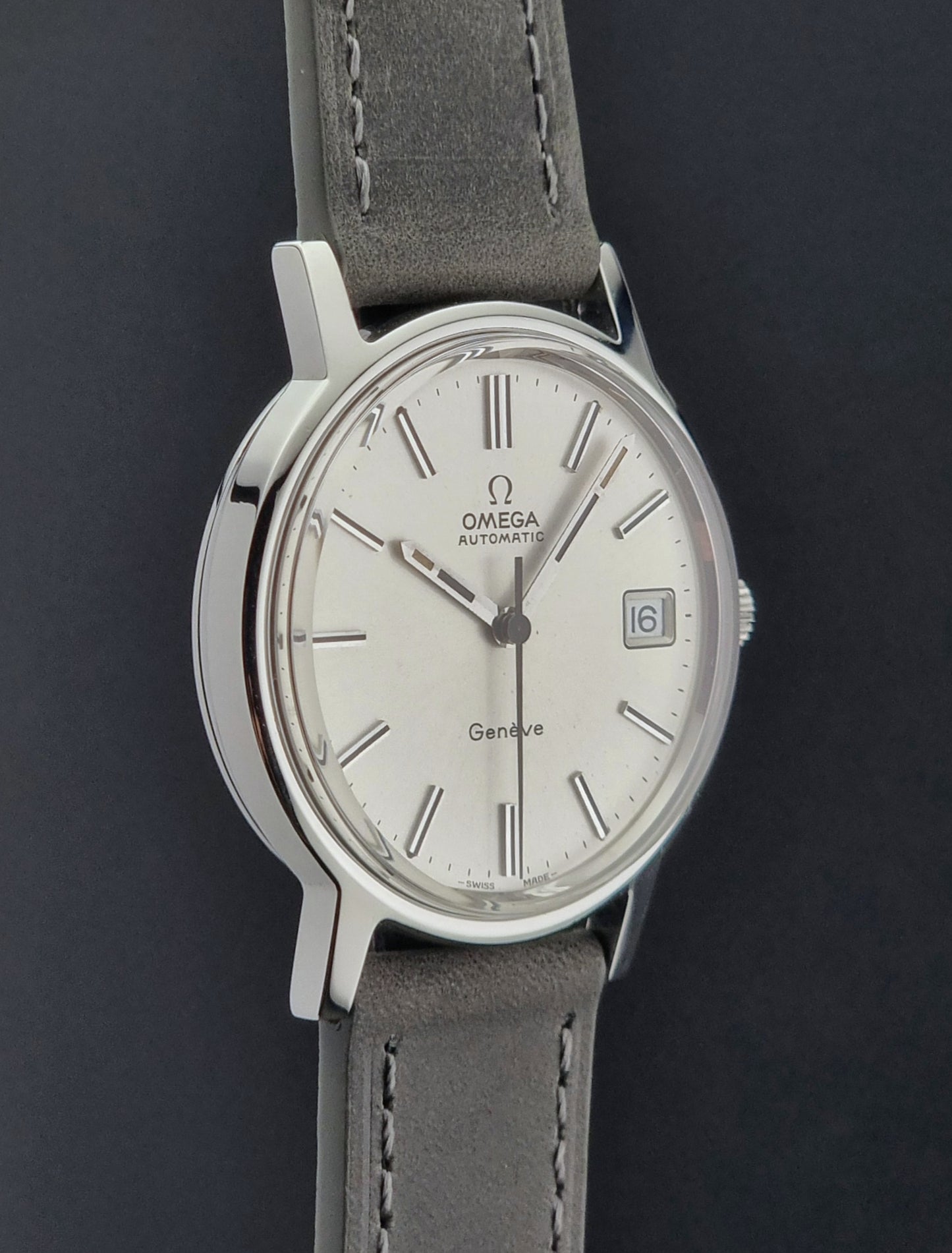 Vintage Omega watch with a silver dial and gray leather strap on a dark background