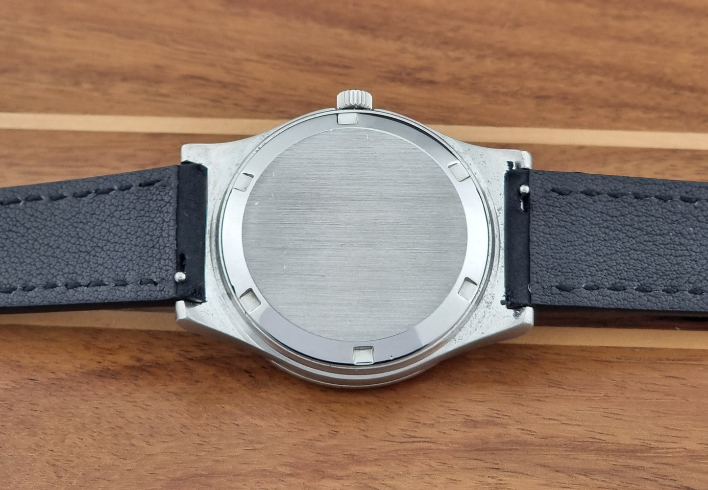 Vintage Omega Geneve 166.0169 wristwatch with a black strap on a wooden surface case back view