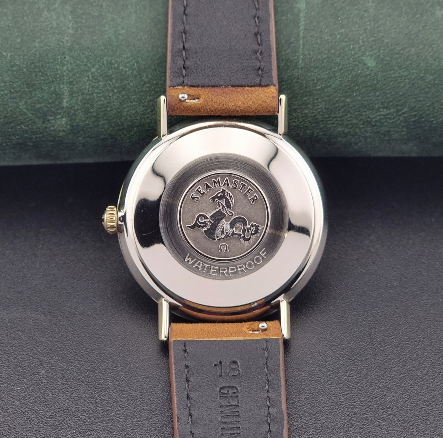 Vintage Omega Seamaster 14735 Gold watch with brown leather strap on a green textured background case back view