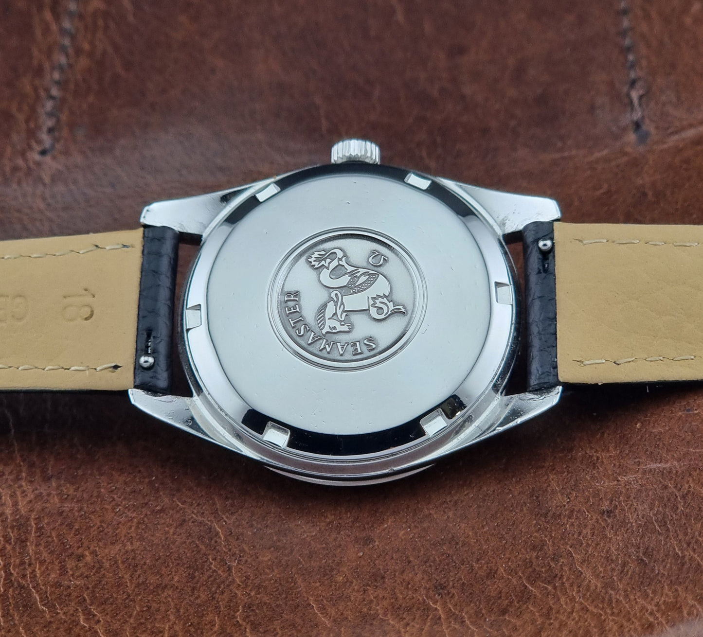 Vintage Omega Seamaster 166.010 watch with a silver dial and black leather strap on a dark surface case back