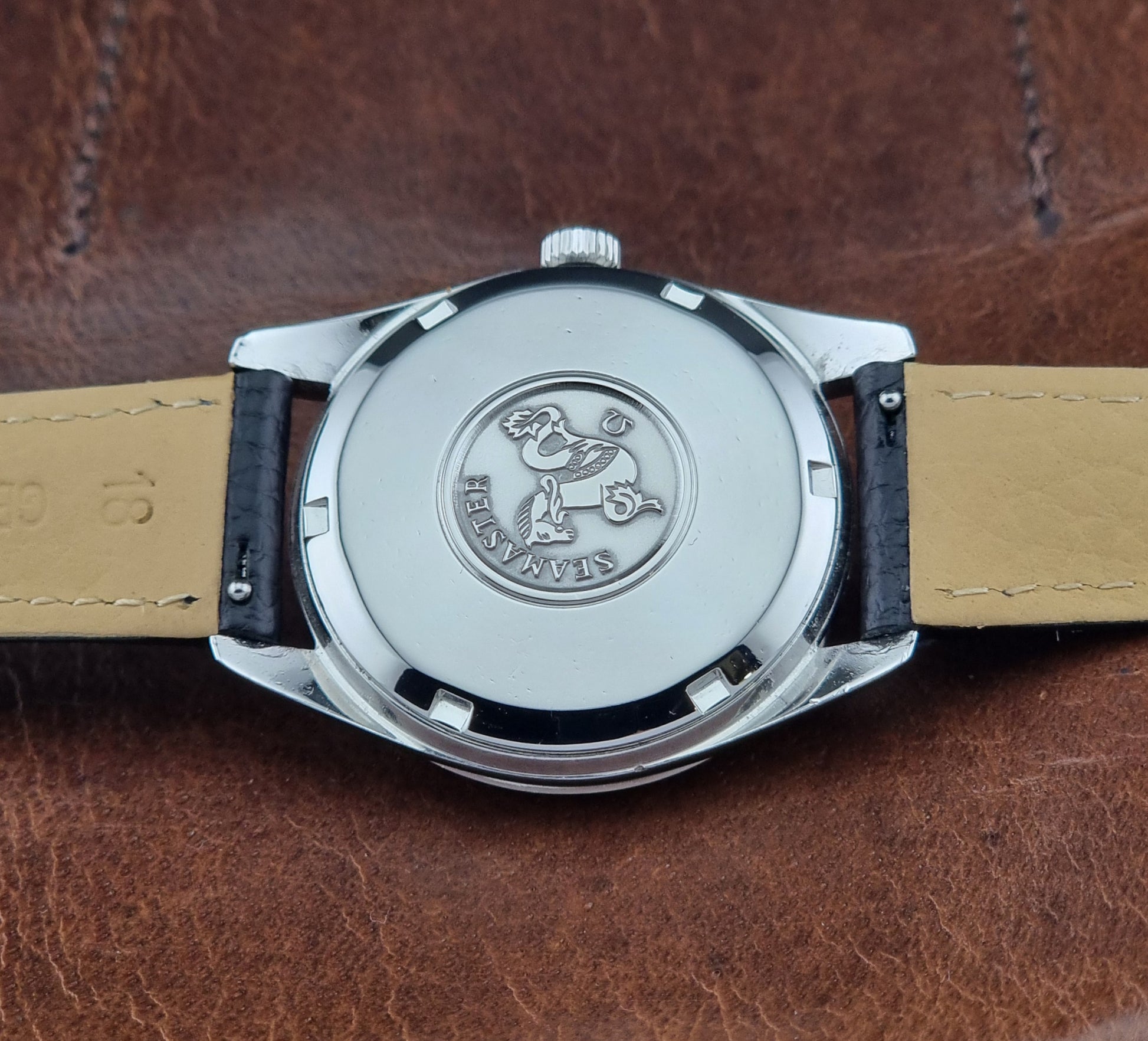 Vintage Omega Seamaster 166.010 watch with a silver dial and black leather strap on a dark surface case back