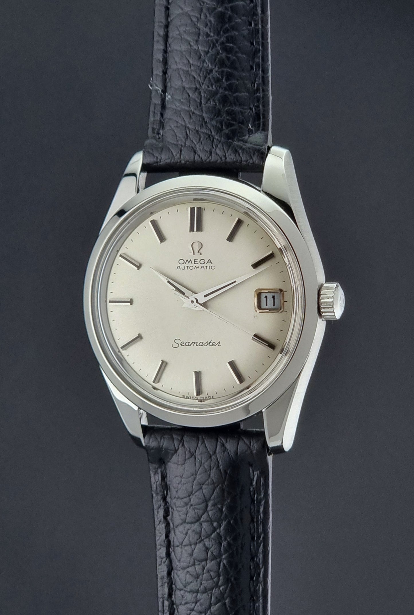 Vintage Omega Seamaster 166.010 watch with a silver dial and black leather strap on a dark surface crown profile