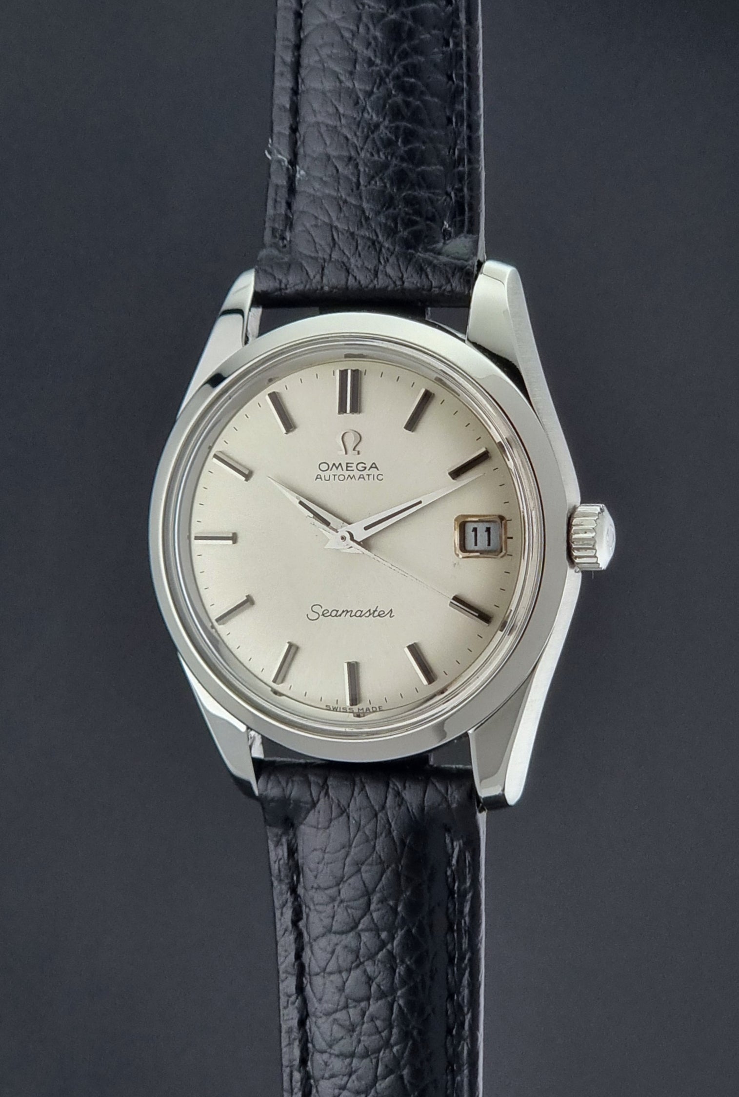 Vintage Omega Seamaster 166.010 watch with a silver dial and black leather strap on a dark surface crown profile