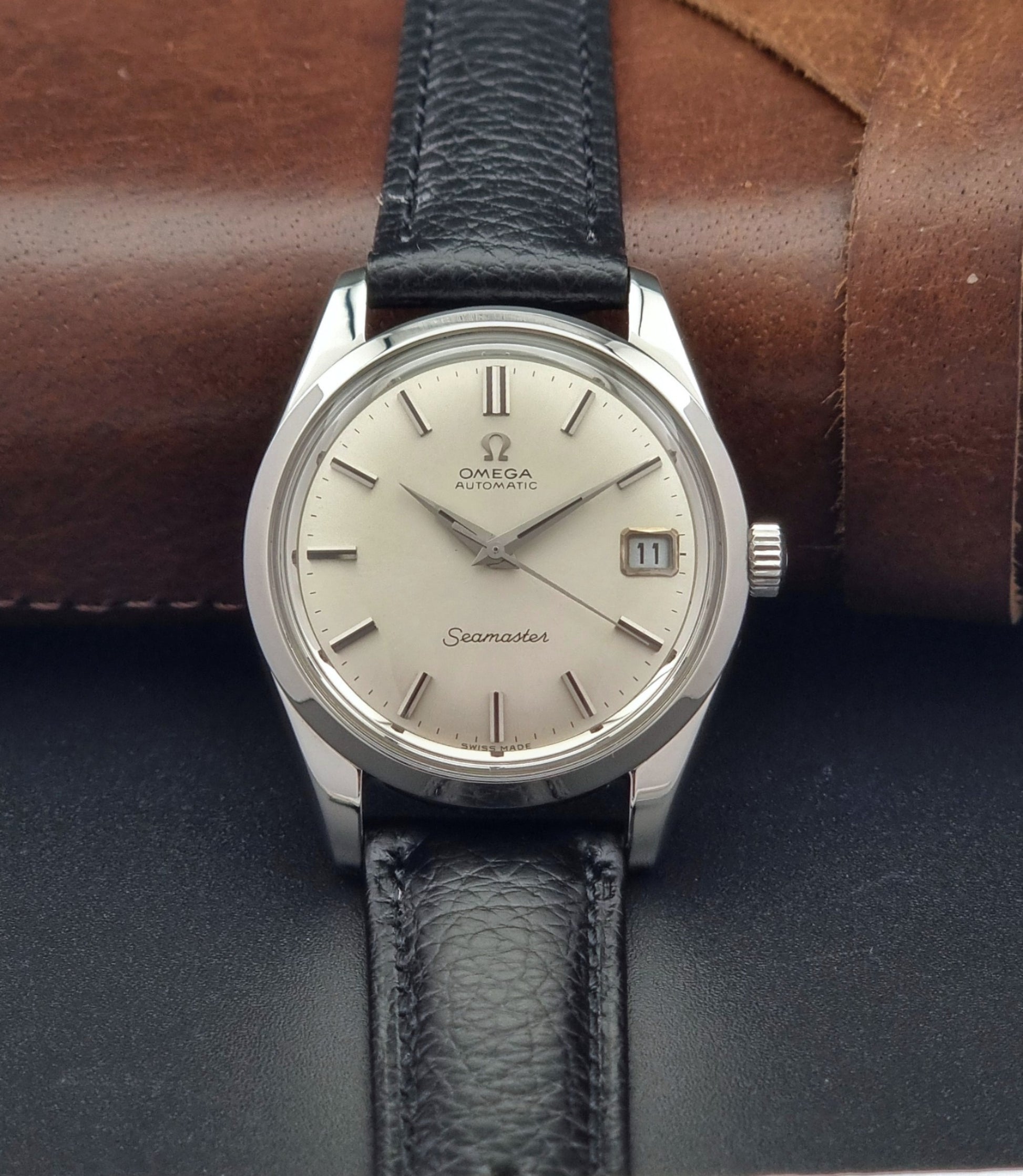Vintage Omega Seamaster 166.010 watch with a silver dial and black leather strap on a dark surface front view