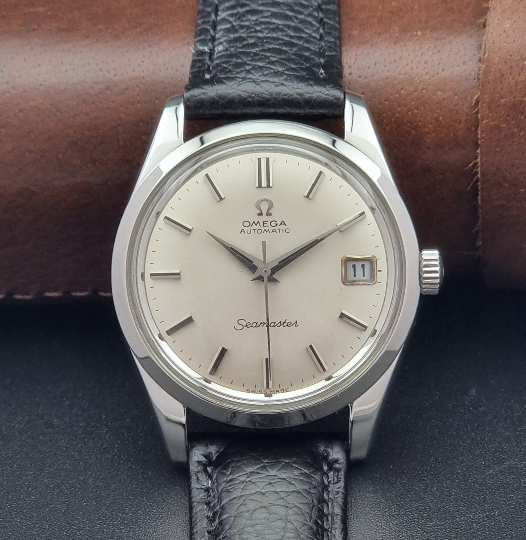 Vintage Omega Seamaster 166.010 watch with a silver dial and black leather strap on a dark surface close up dial view