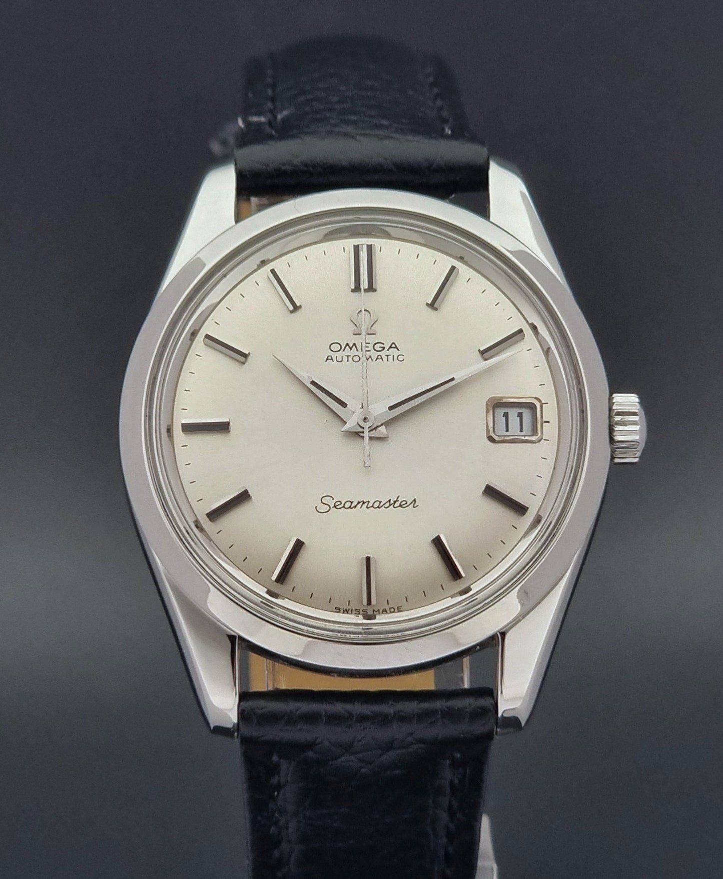 Vintage Omega Seamaster 166.010 watch with a silver dial and black leather strap on a dark surface close up