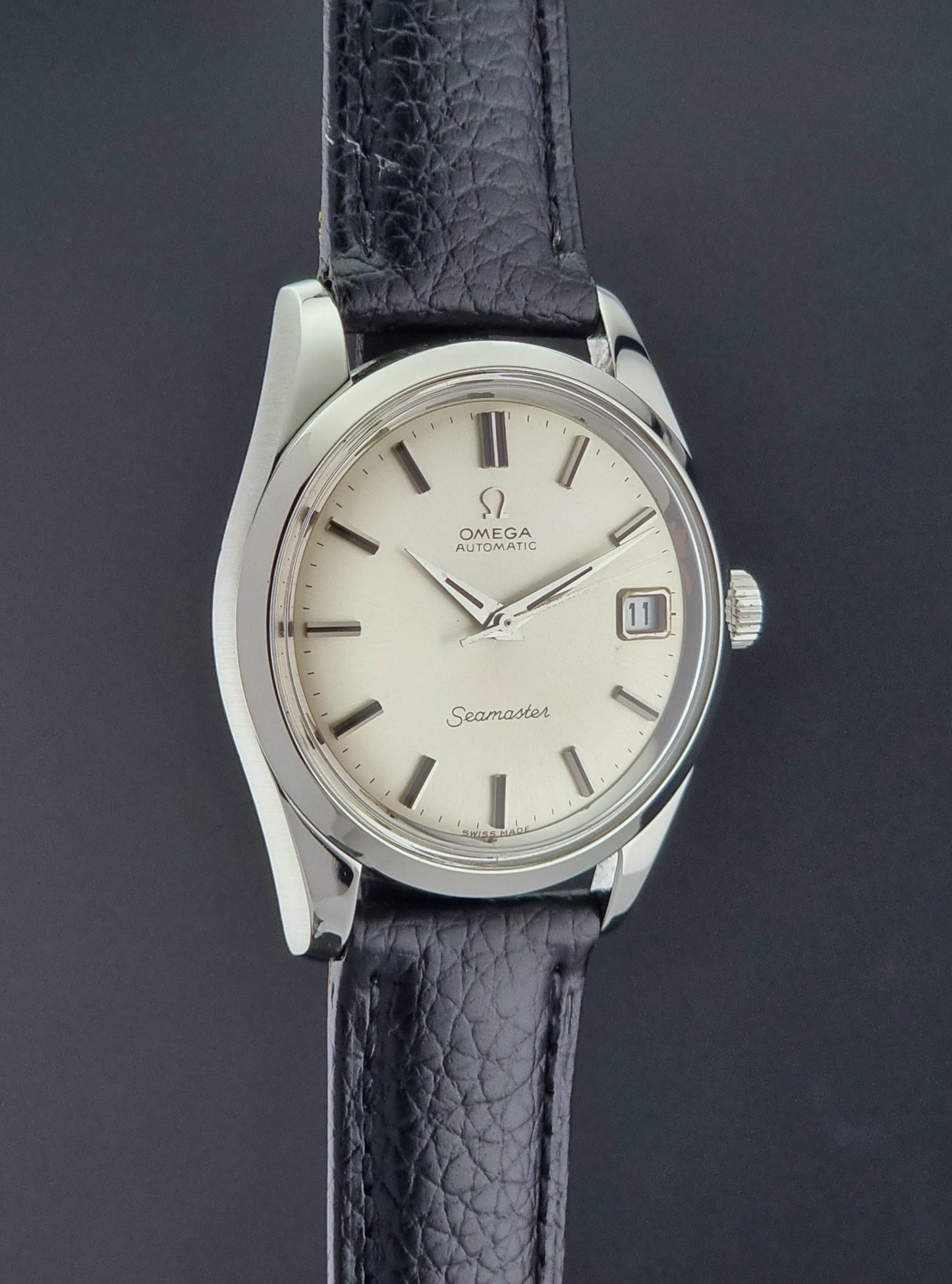 Vintage Omega Seamaster 166.010 watch with a silver dial and black leather strap on a dark surface side profile