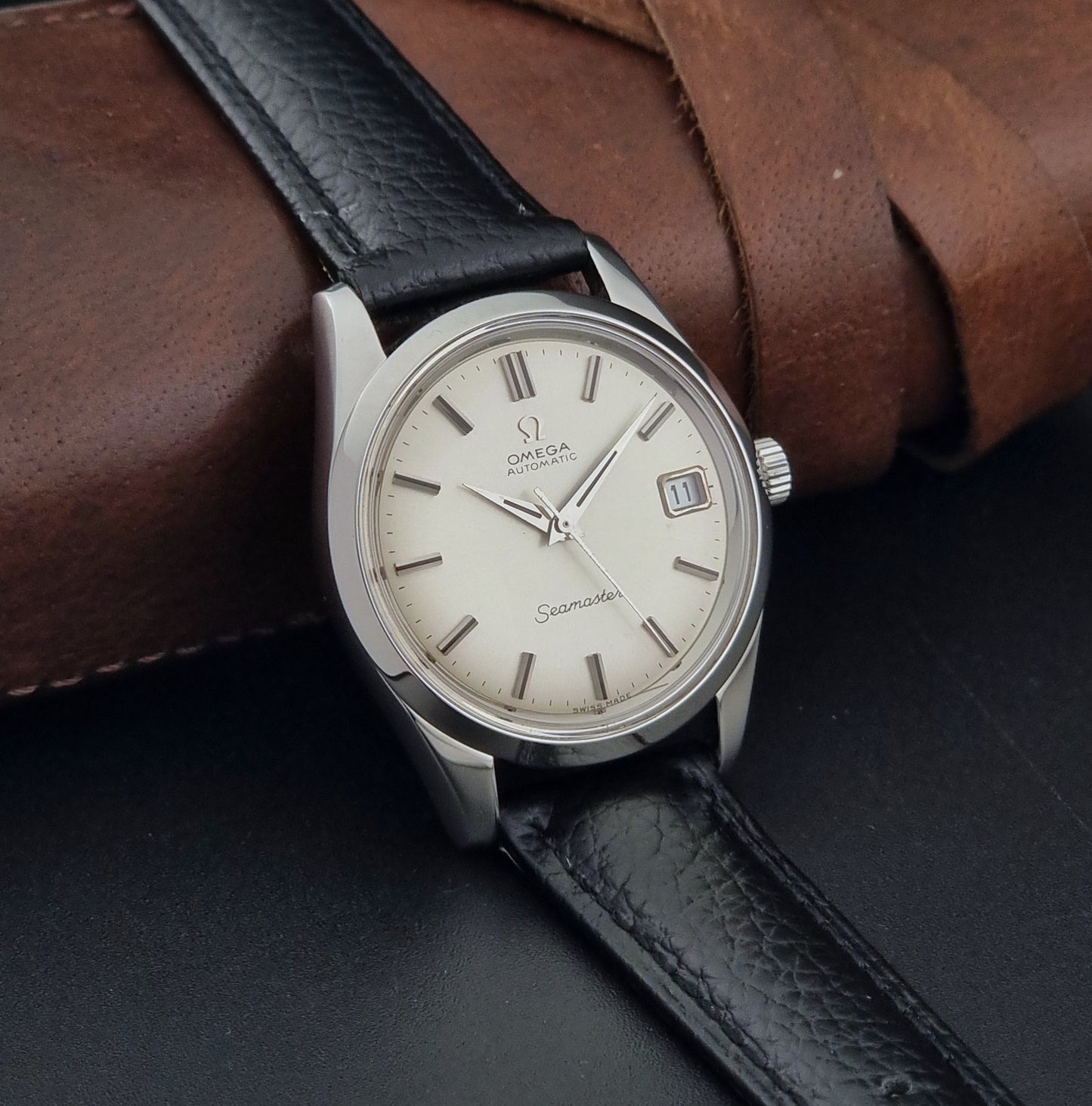 Vintage Omega Seamaster 166.010 watch with a silver dial and black leather strap on a dark surface side view