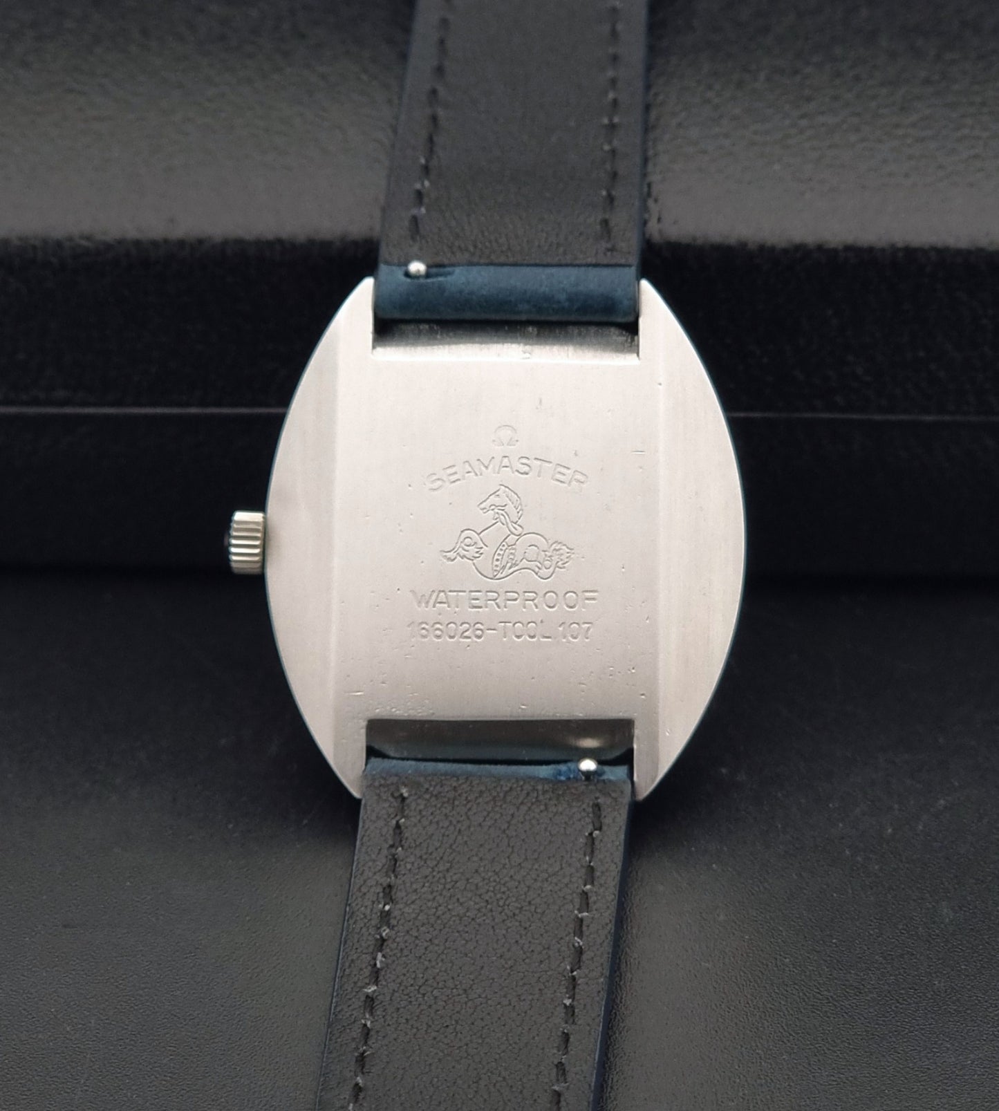 Vintage Omega 166.026 Seamaster Cosmic Wristwatch with blue leather strap and silver case on a dark gray background back view