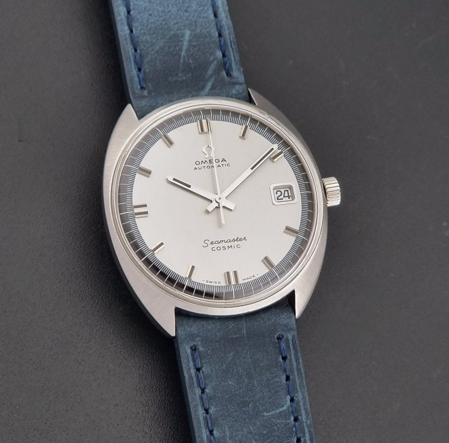 Vintage Omega 166.026 Seamaster Cosmic Wristwatch with blue leather strap and silver case on a dark gray background front view