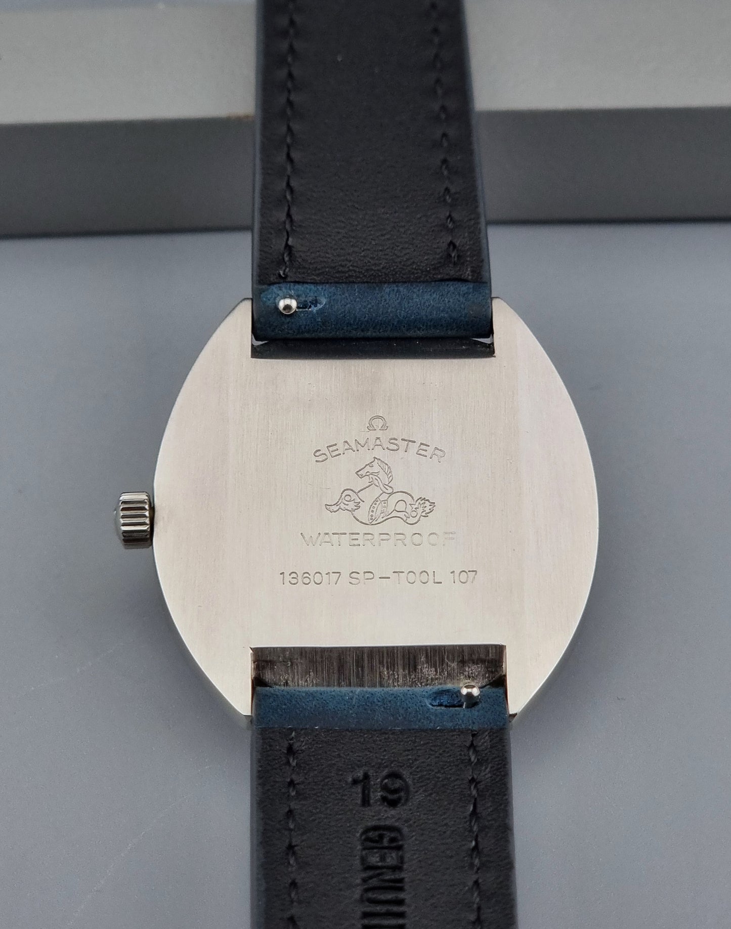 Vintage Omega Seamaster Cosmic wristwatch with blue strap and silver case on a gray background back view