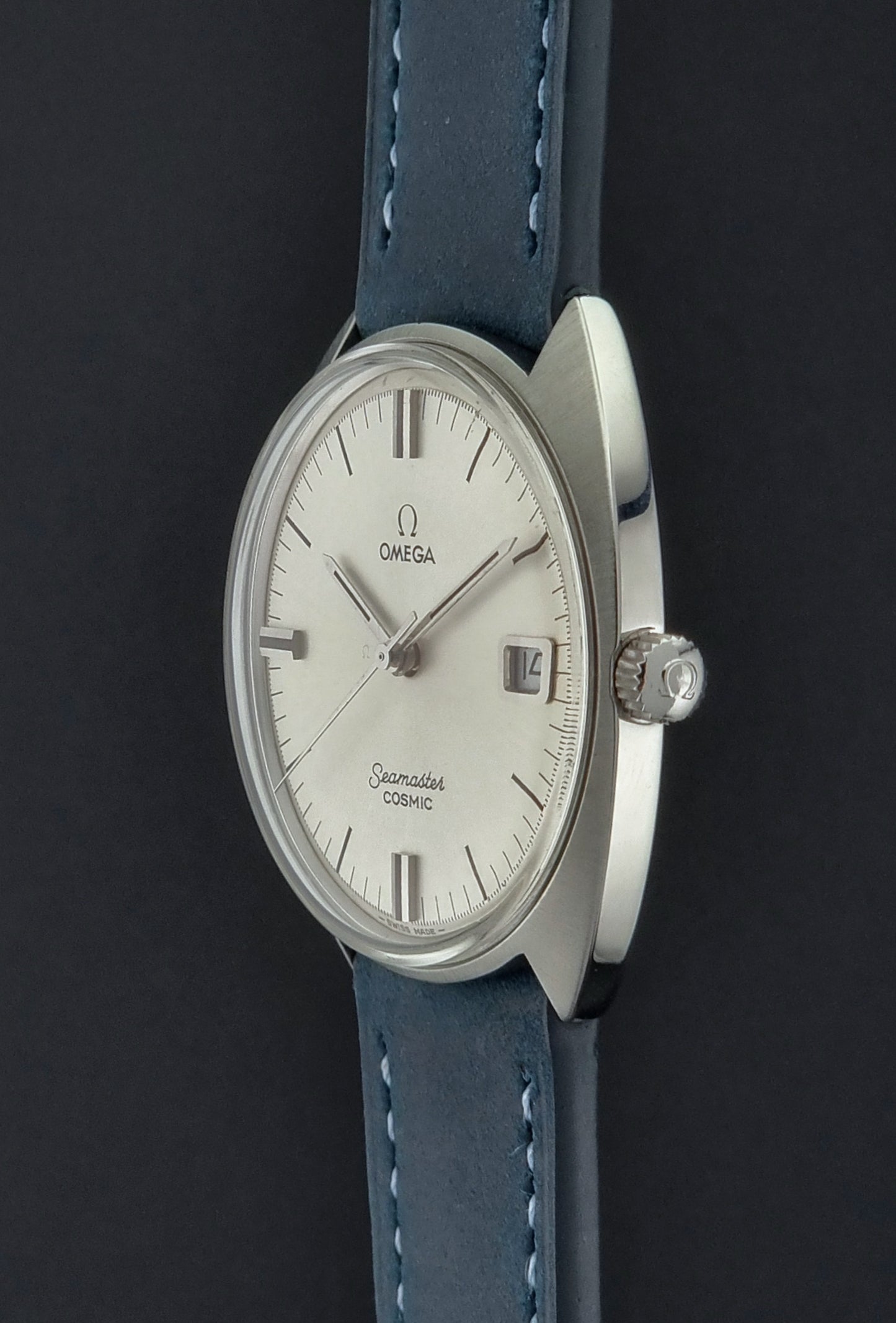 Vintage Omega Seamaster Cosmic wristwatch with blue strap and silver case on a gray background crown view