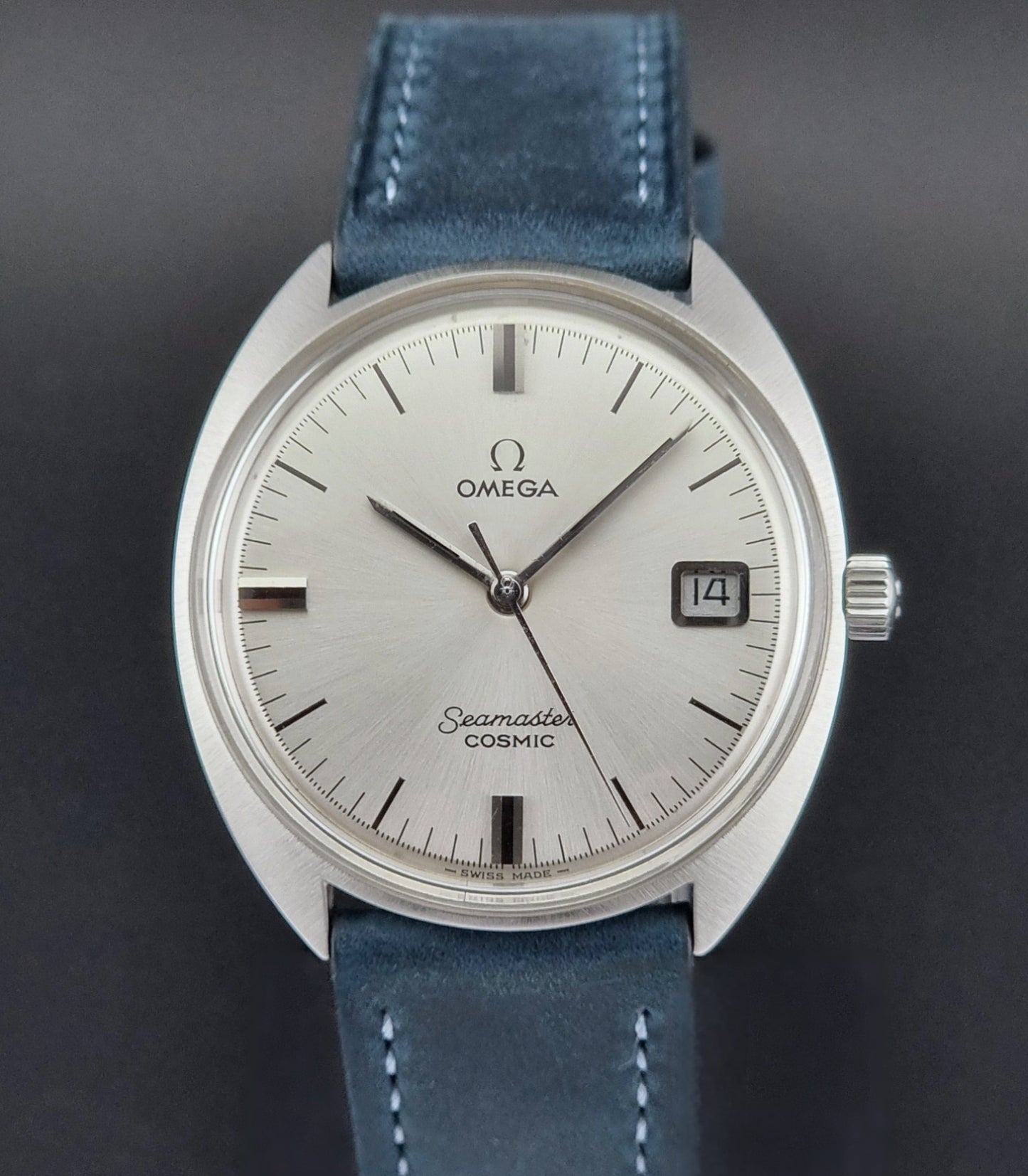 Vintage Omega Seamaster Cosmic wristwatch with blue strap and silver case on a gray background front view