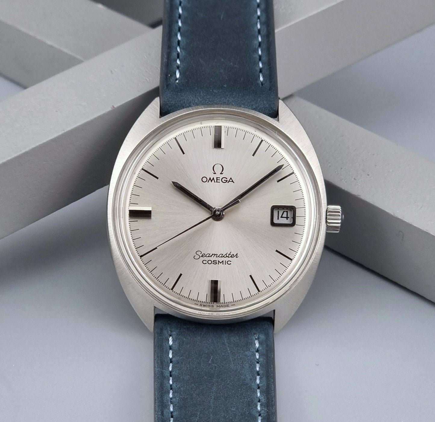 Vintage Omega Seamaster Cosmic wristwatch with blue strap and silver case on a gray background front view