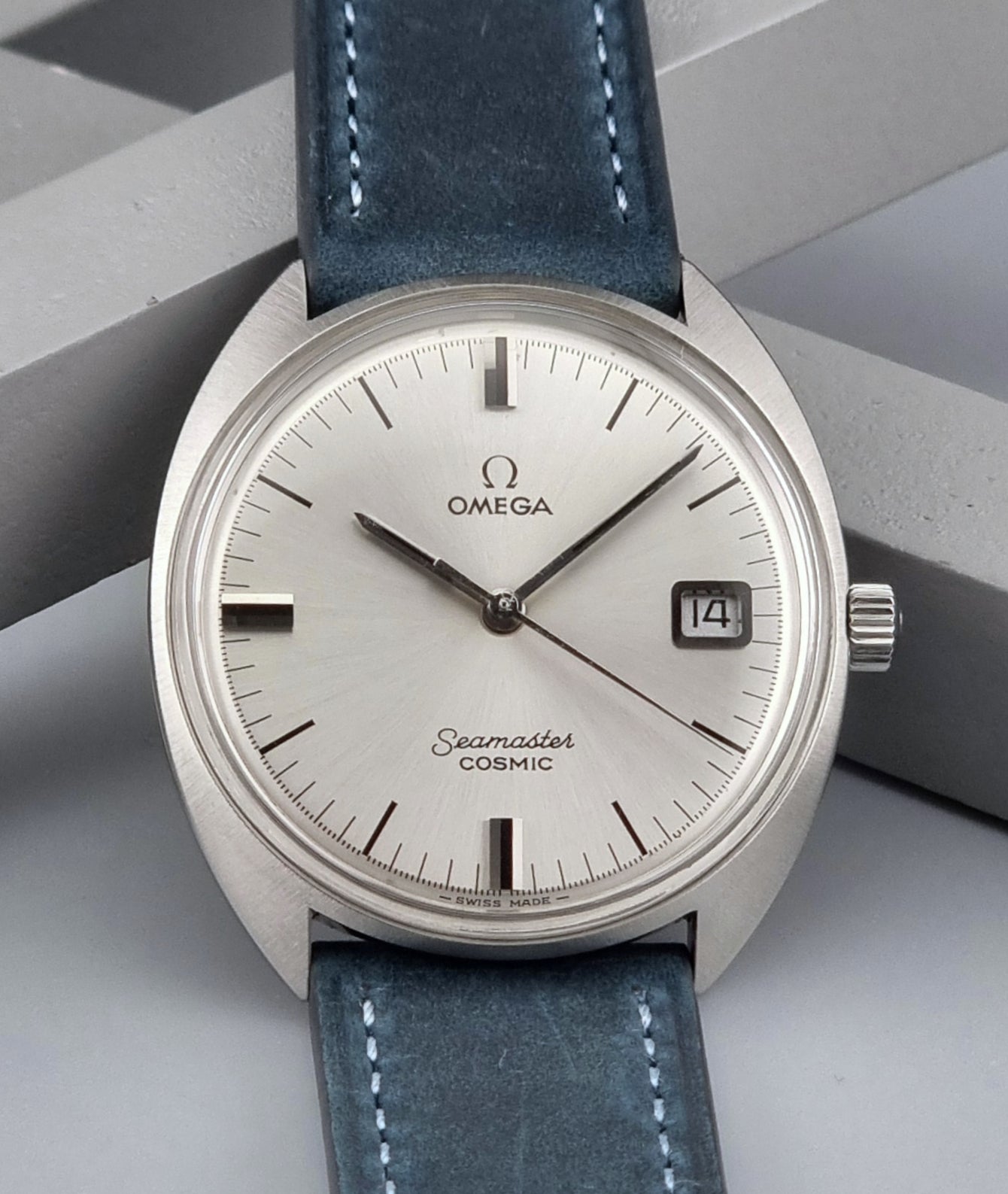 Vintage Omega Seamaster Cosmic wristwatch with blue strap and silver case on a gray background front view