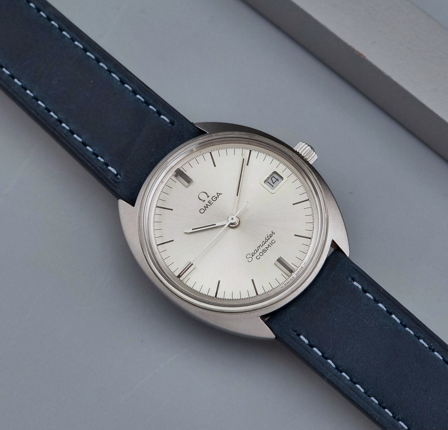 Vintage Omega Seamaster Cosmic wristwatch with blue strap and silver case on a gray background front view