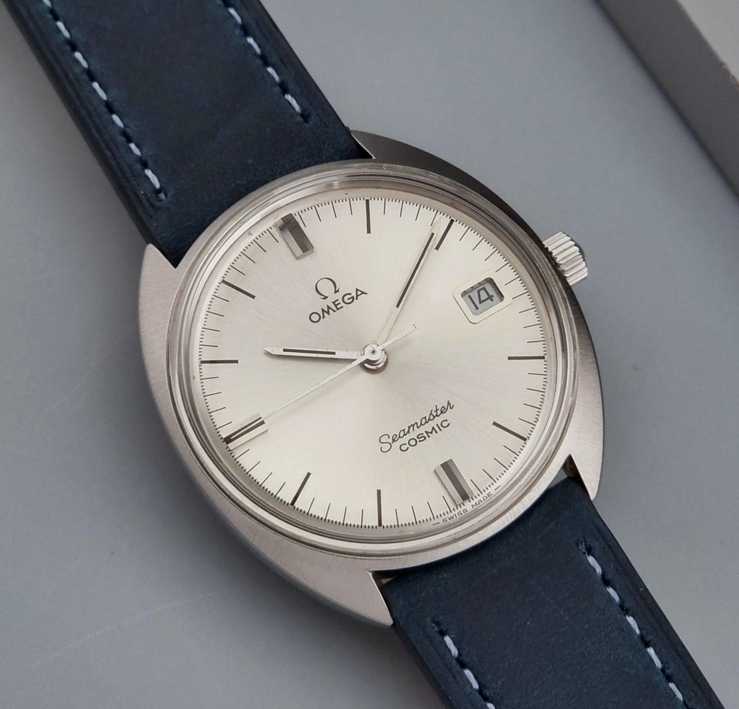 Vintage Omega Seamaster Cosmic wristwatch with blue strap and silver case on a gray background front view