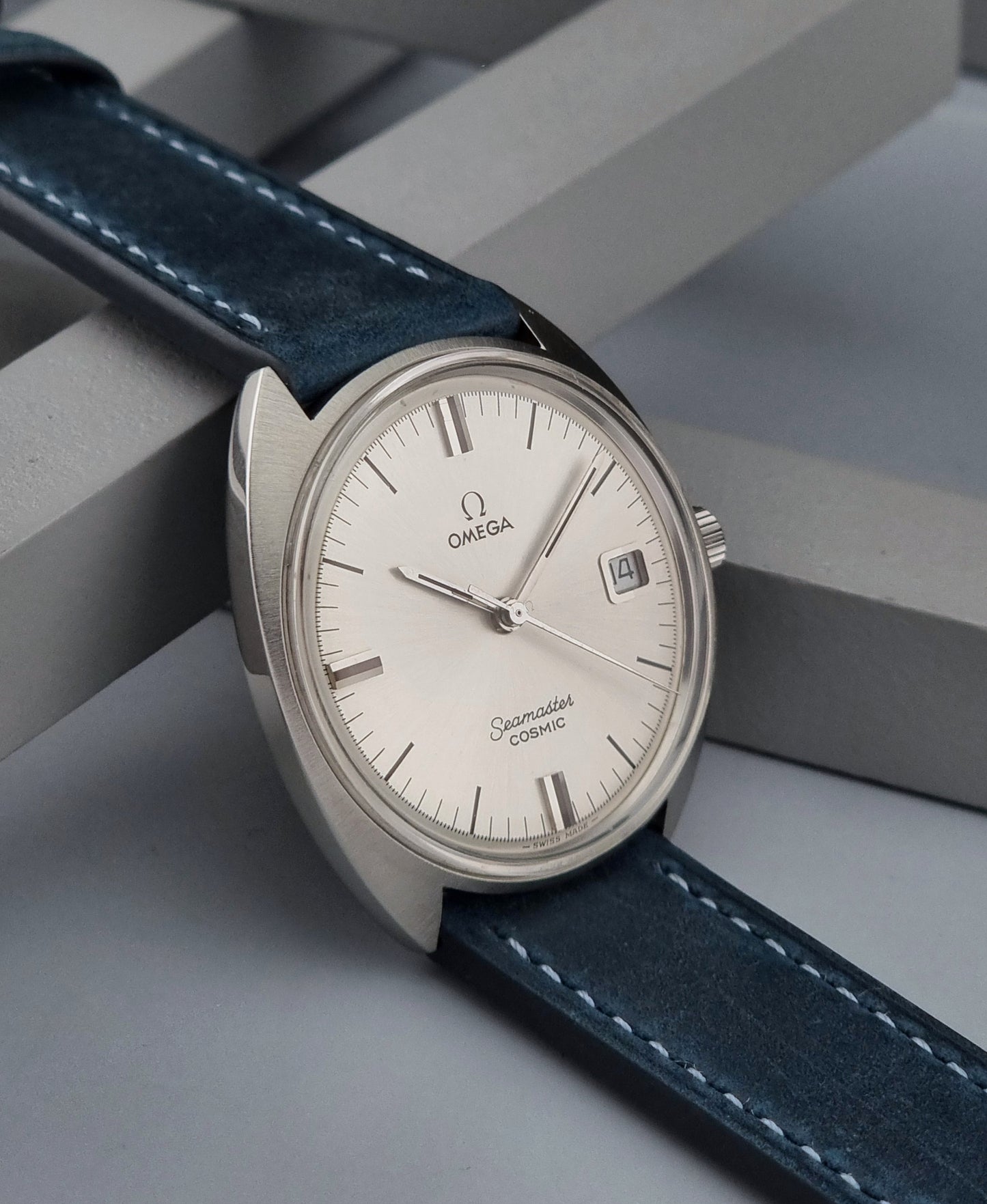 Vintage Omega Seamaster Cosmic wristwatch with blue strap and silver case on a gray background side view