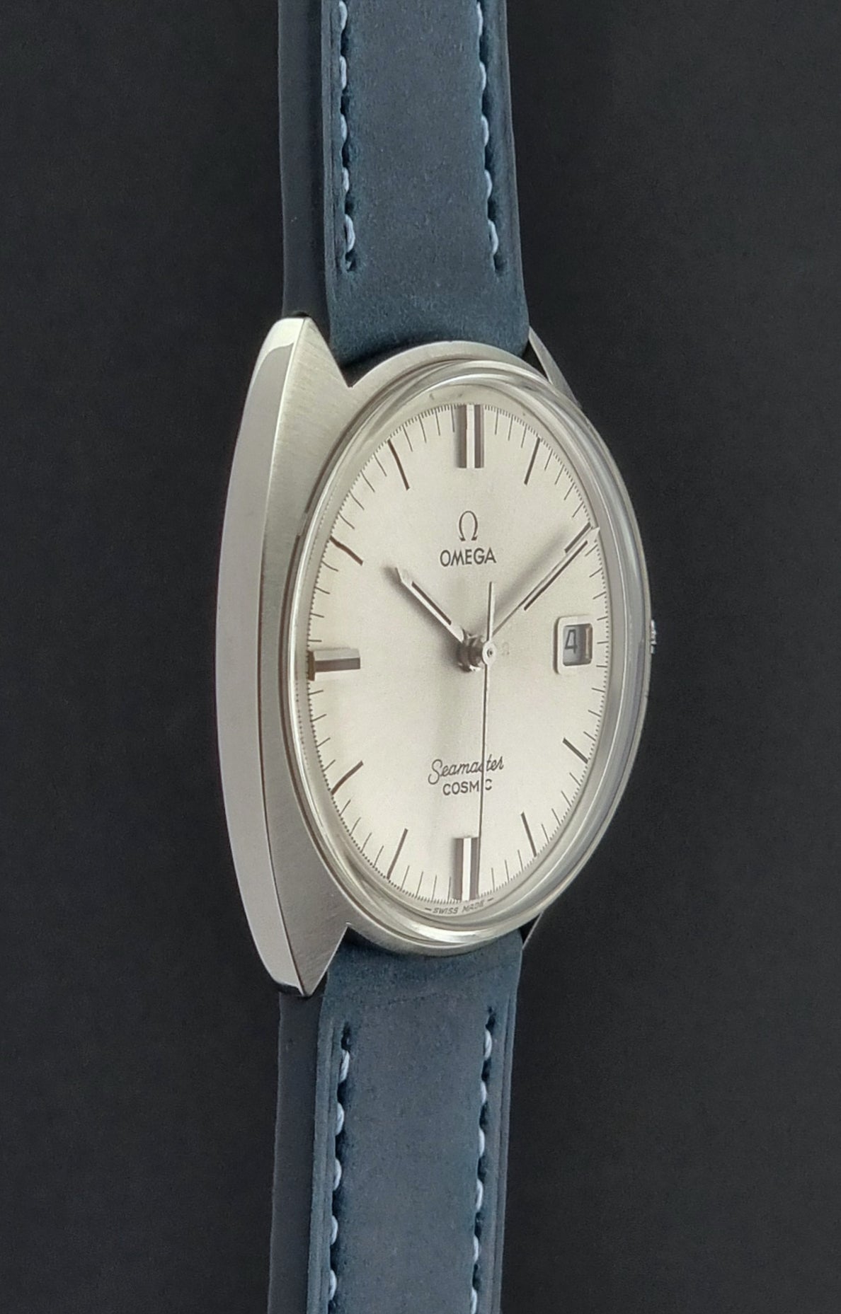 Vintage Omega Seamaster Cosmic wristwatch with blue strap and silver case on a gray background side view