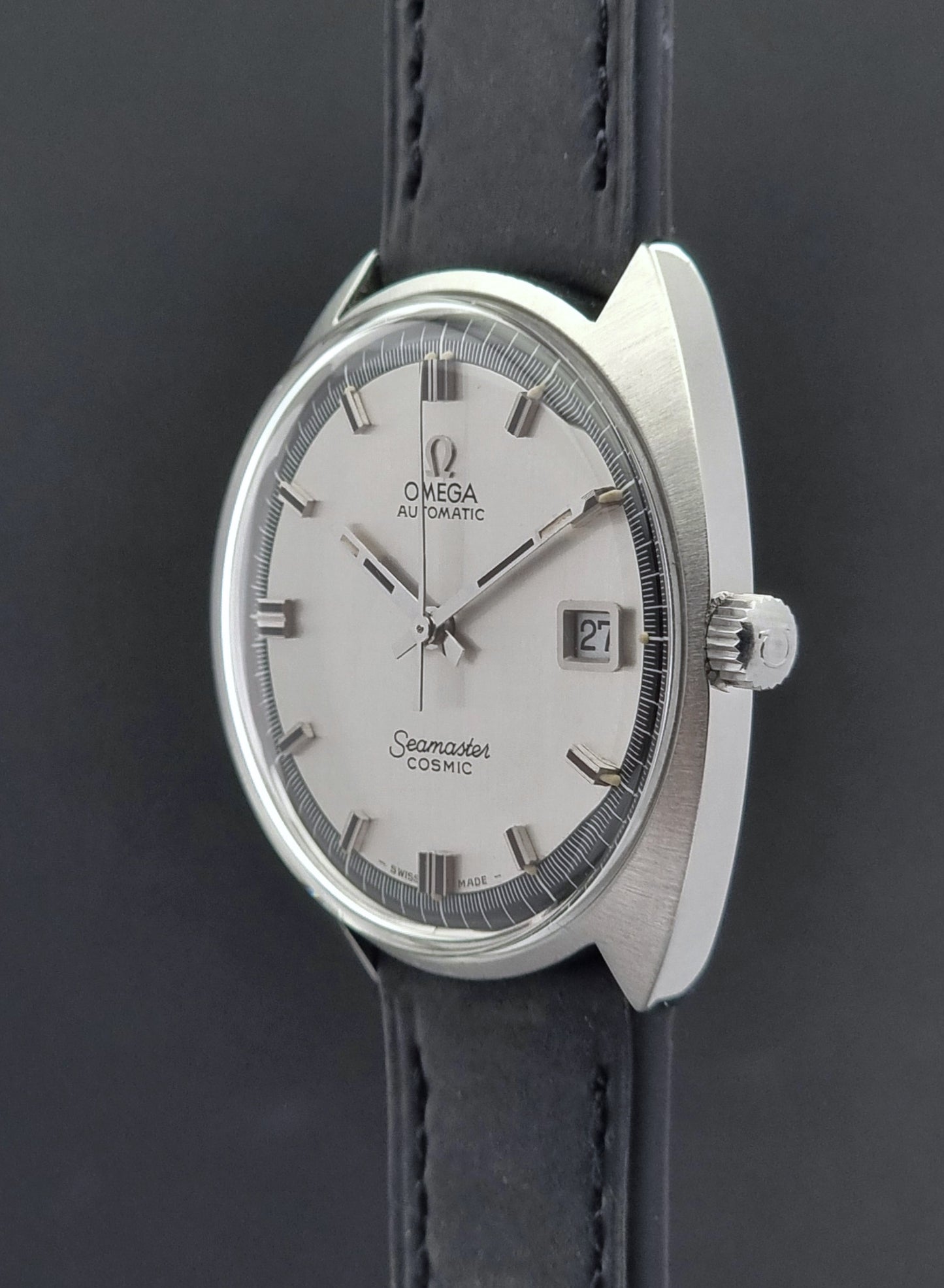 crown side view of a Vintage Omega Seamaster Cosmic watch with silver dial and black leather strap on a dark background