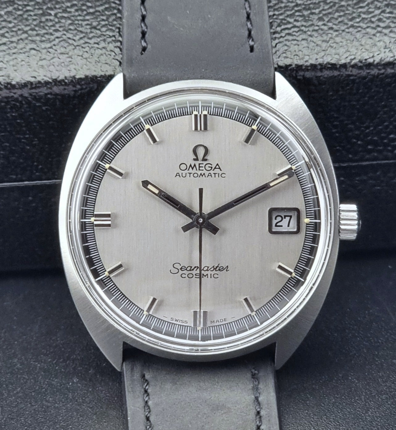 Front view of a Omega Seamaster Cosmic watch with silver dial and gray leather strap on a dark background