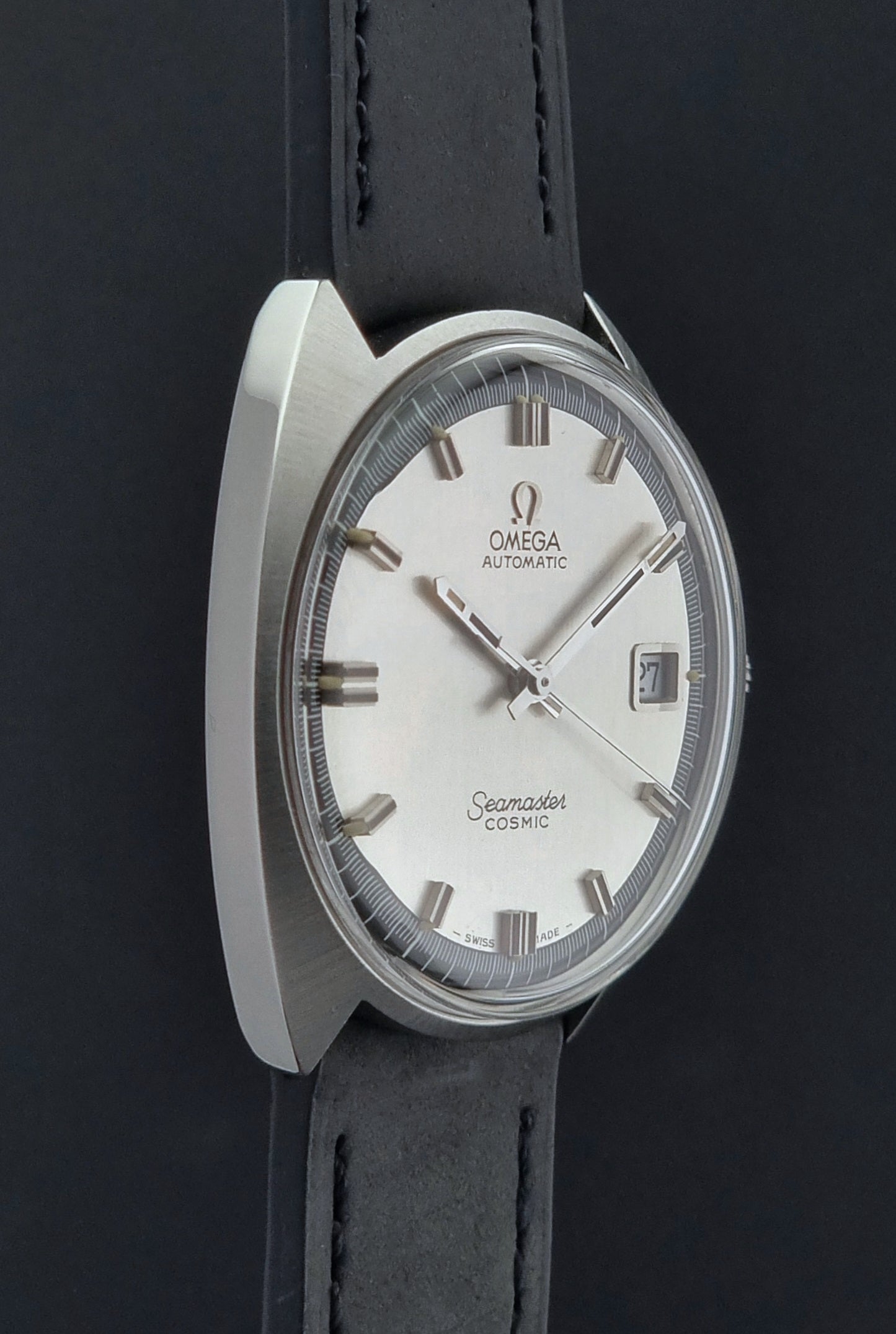 side view of a Vintage Omega Seamaster Cosmic watch with black strap and silver case on a dark background