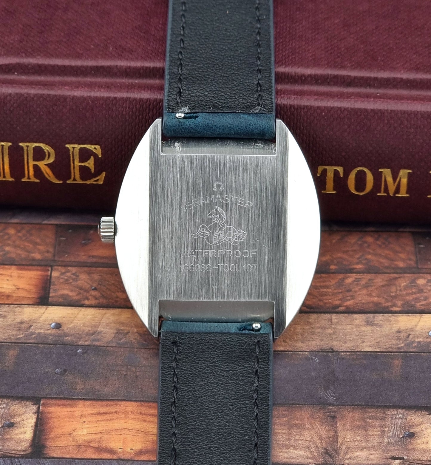 Vintage Omega Seamaster Cosmic Close-up of the watch case back with a black leather strap on a wooden surface