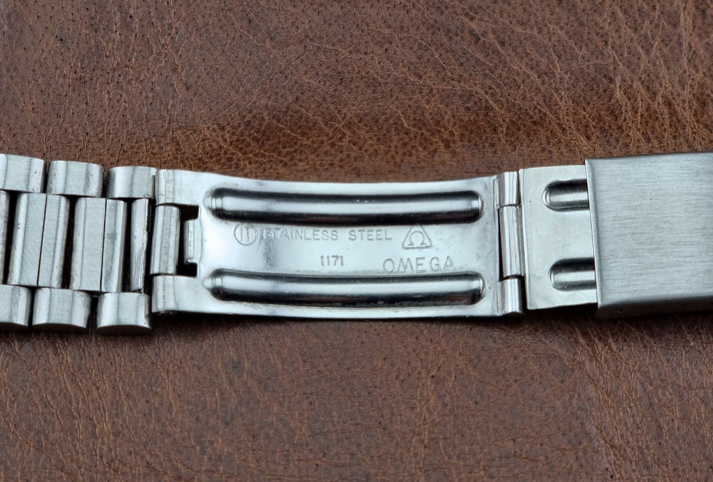Metallic watch band with Omega branding on a brown leather background