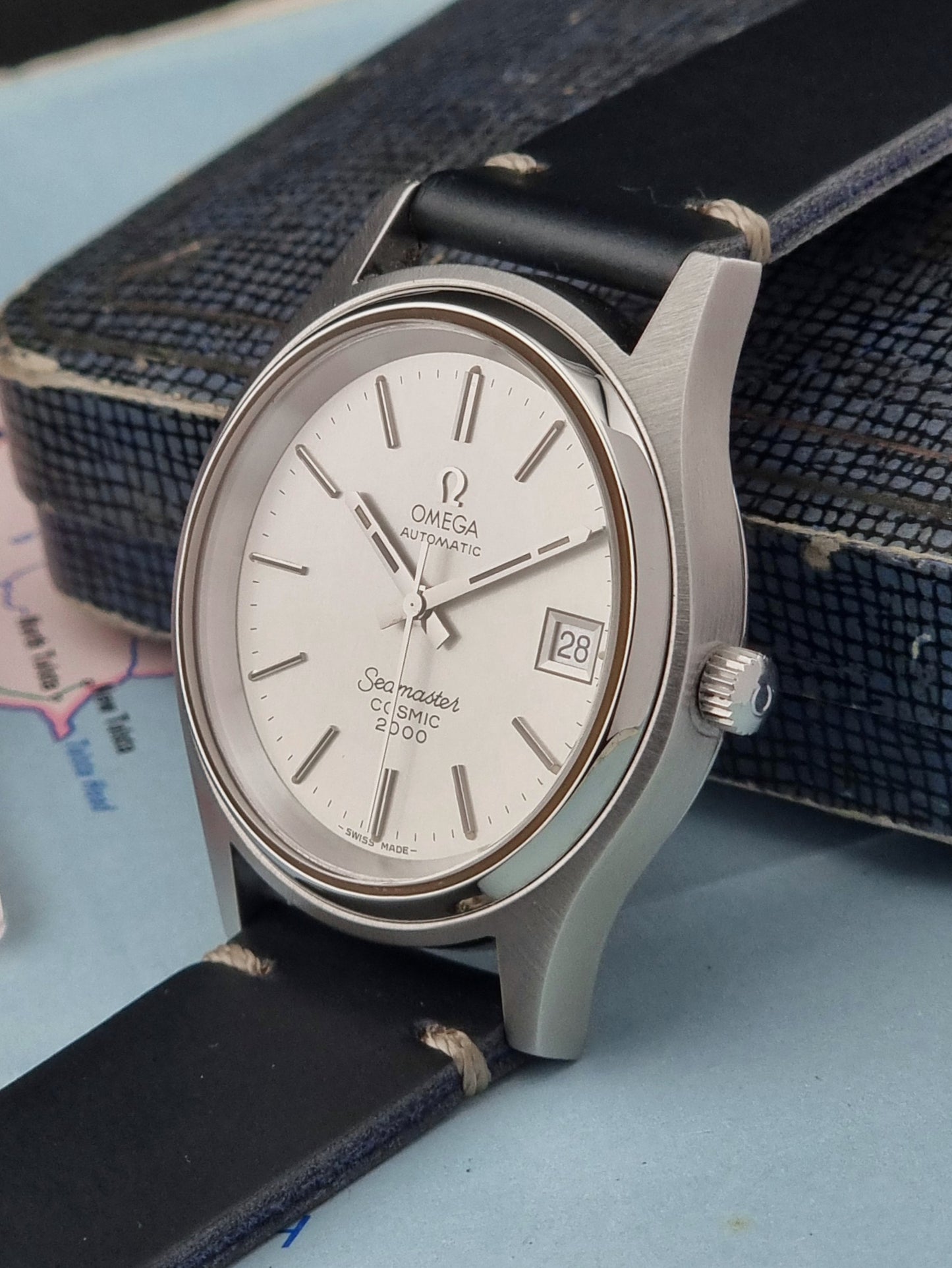 Omega Seamaster Cosmic 2000 166.128 watch with a silver case and black leather strap on a textured surface