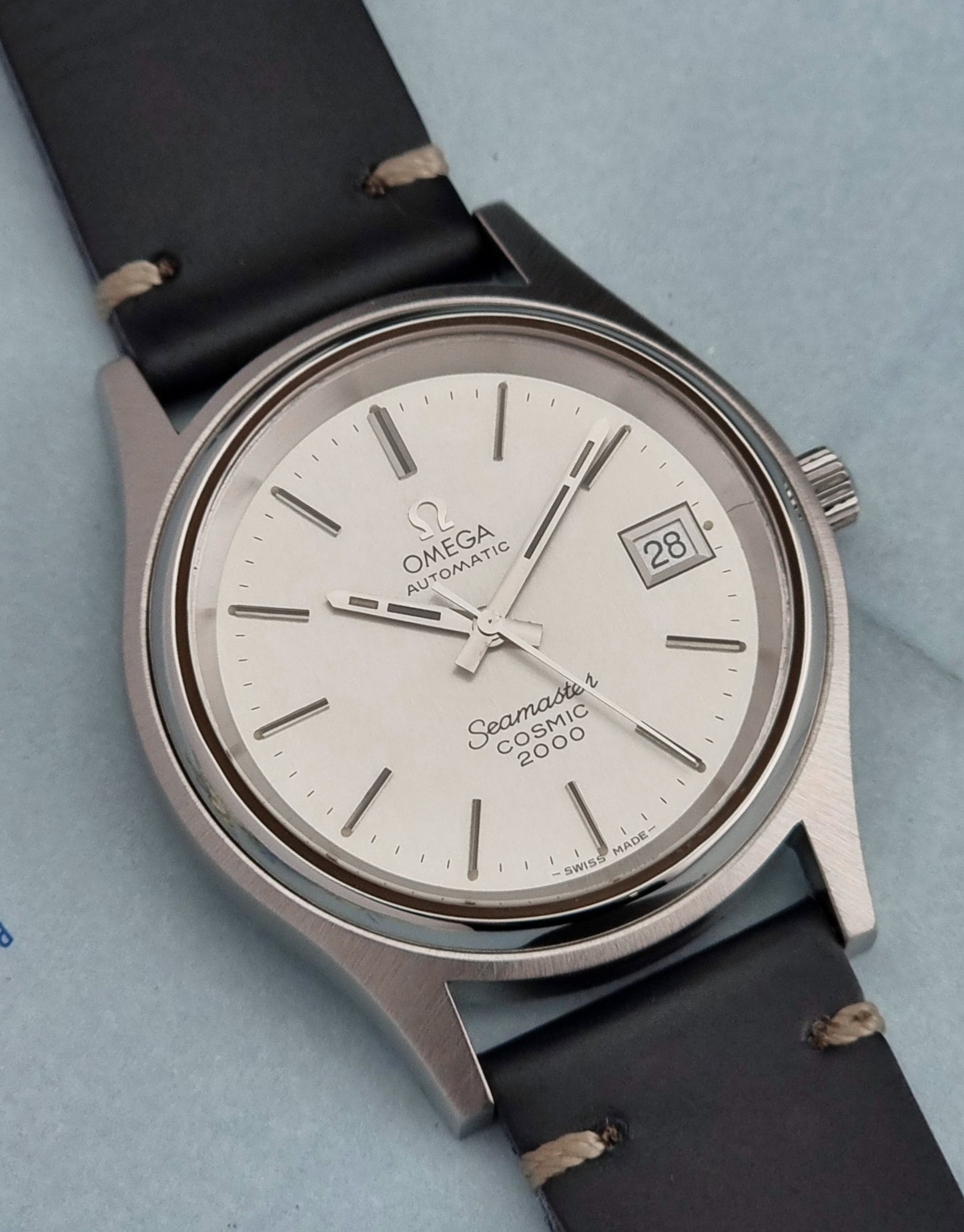 Omega Seamaster Cosmic 2000 166.128 watch with a black leather strap on a light blue background