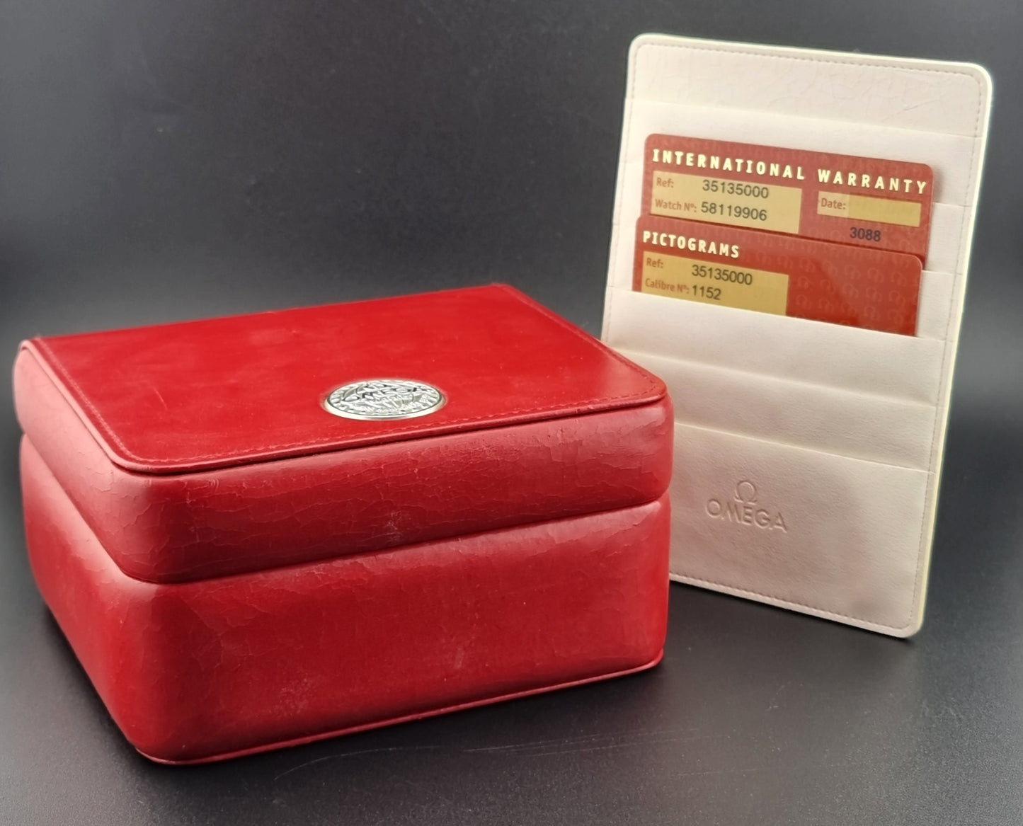 Red watch box with Omega logo and warranty card on a dark background