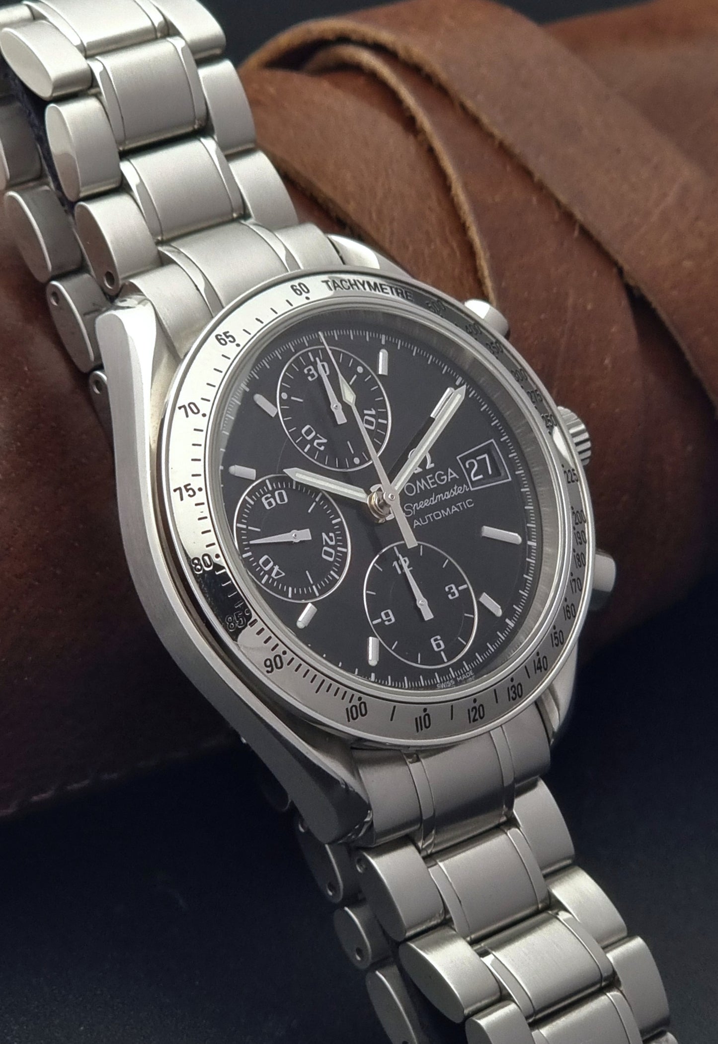 Omega Speedmaster wristwatch with a dark face on a brown leather background