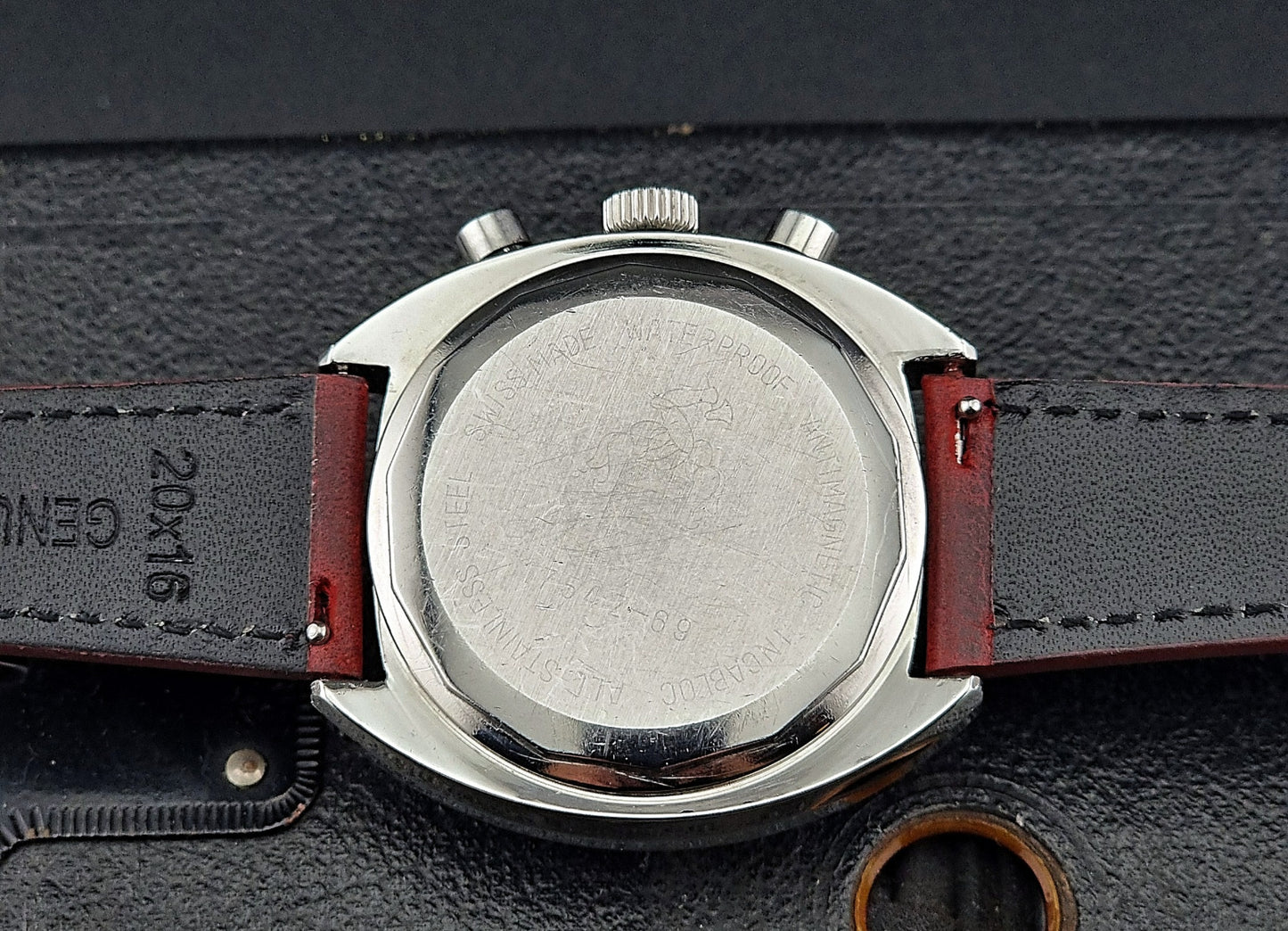 Close-up of watch case back with a brown leather strap on a dark background