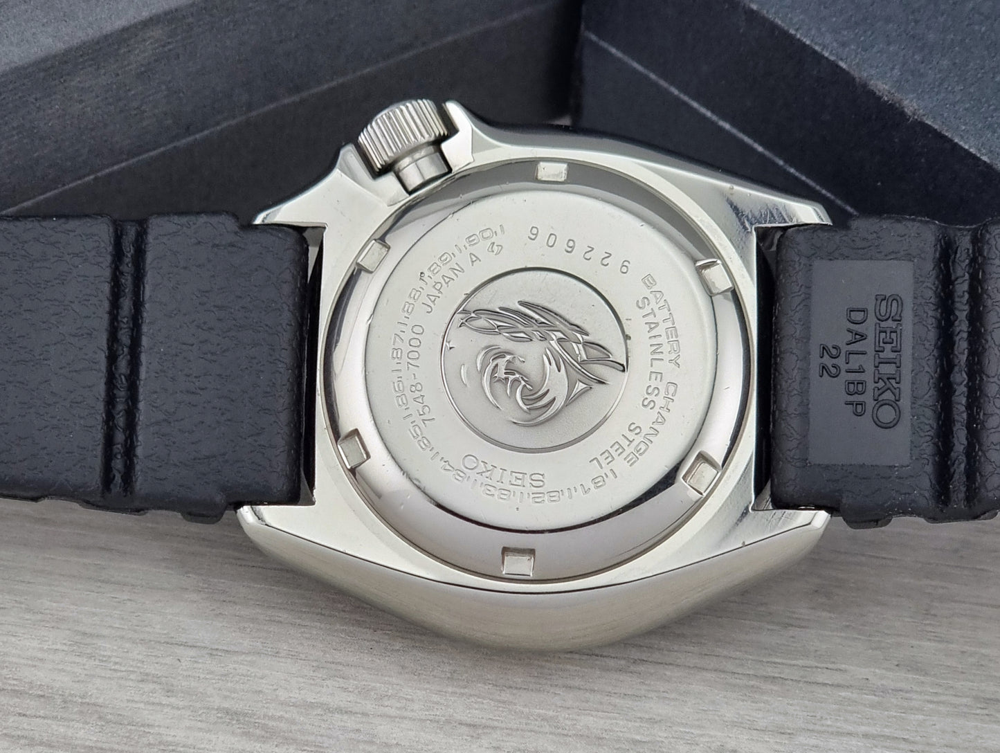 Close-up of a watch case with brand logo on a gray surface