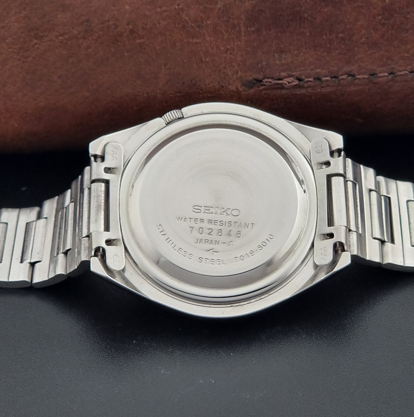 Vintage Seiko Actus Wristwatch 7019-8010 with a Black dial and bracelet on a dark back ground case back view